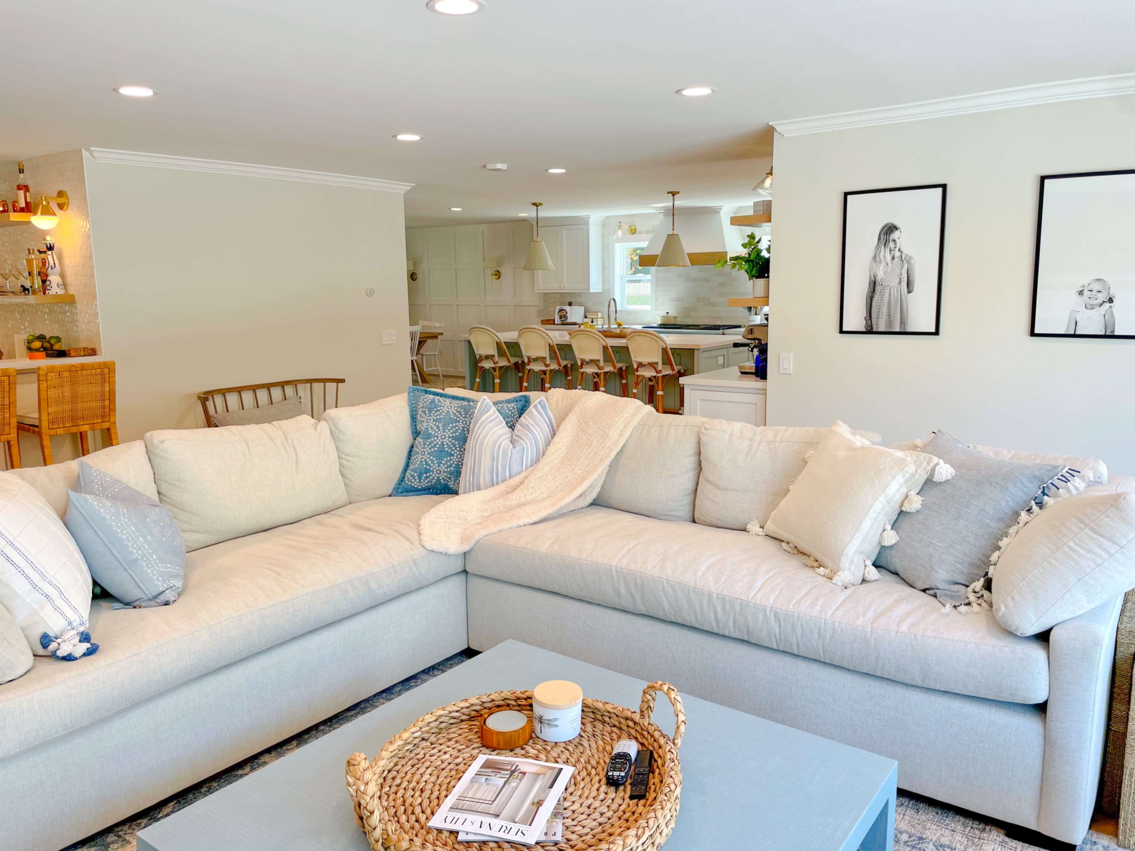 A light-colored sectional sofa with decorative pillows in a bright living room that connects to a kitchen with bar seating.