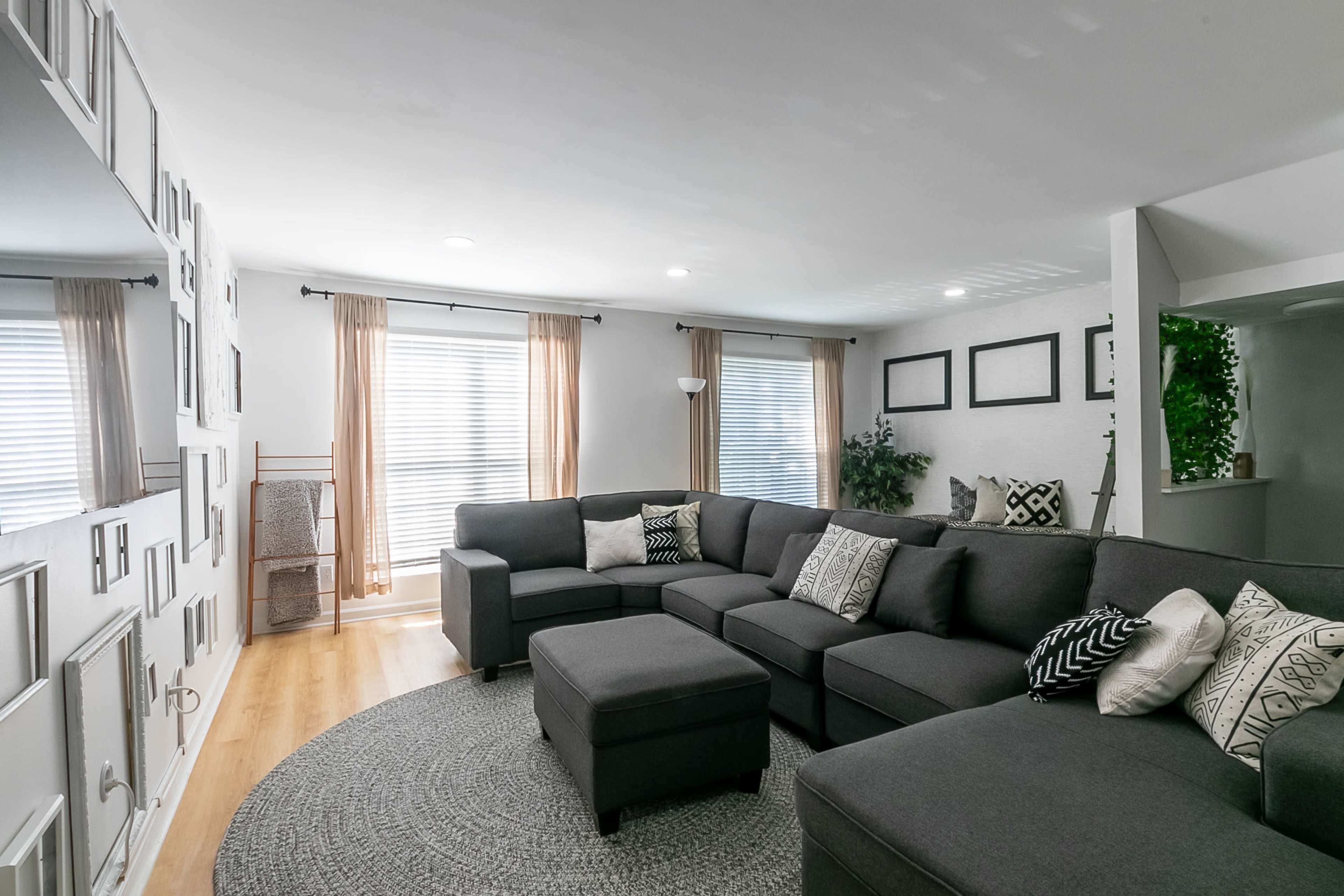 A spacious living room features a large sectional sofa, a circular rug, and several framed pictures on the wall.