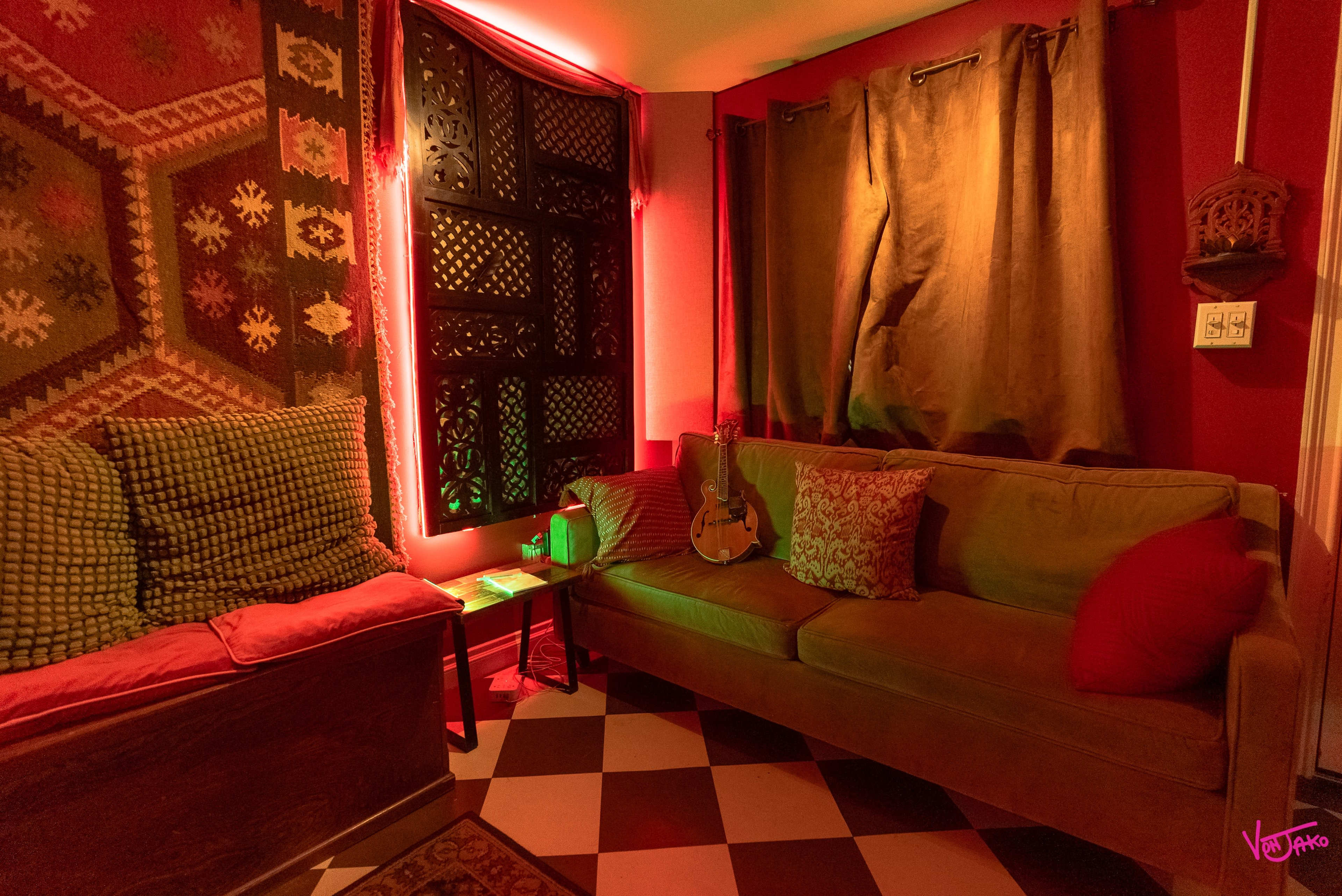 The room features a cozy seating area with a guitar resting on a couch, surrounded by patterned textiles and softly illuminated by red lighting.