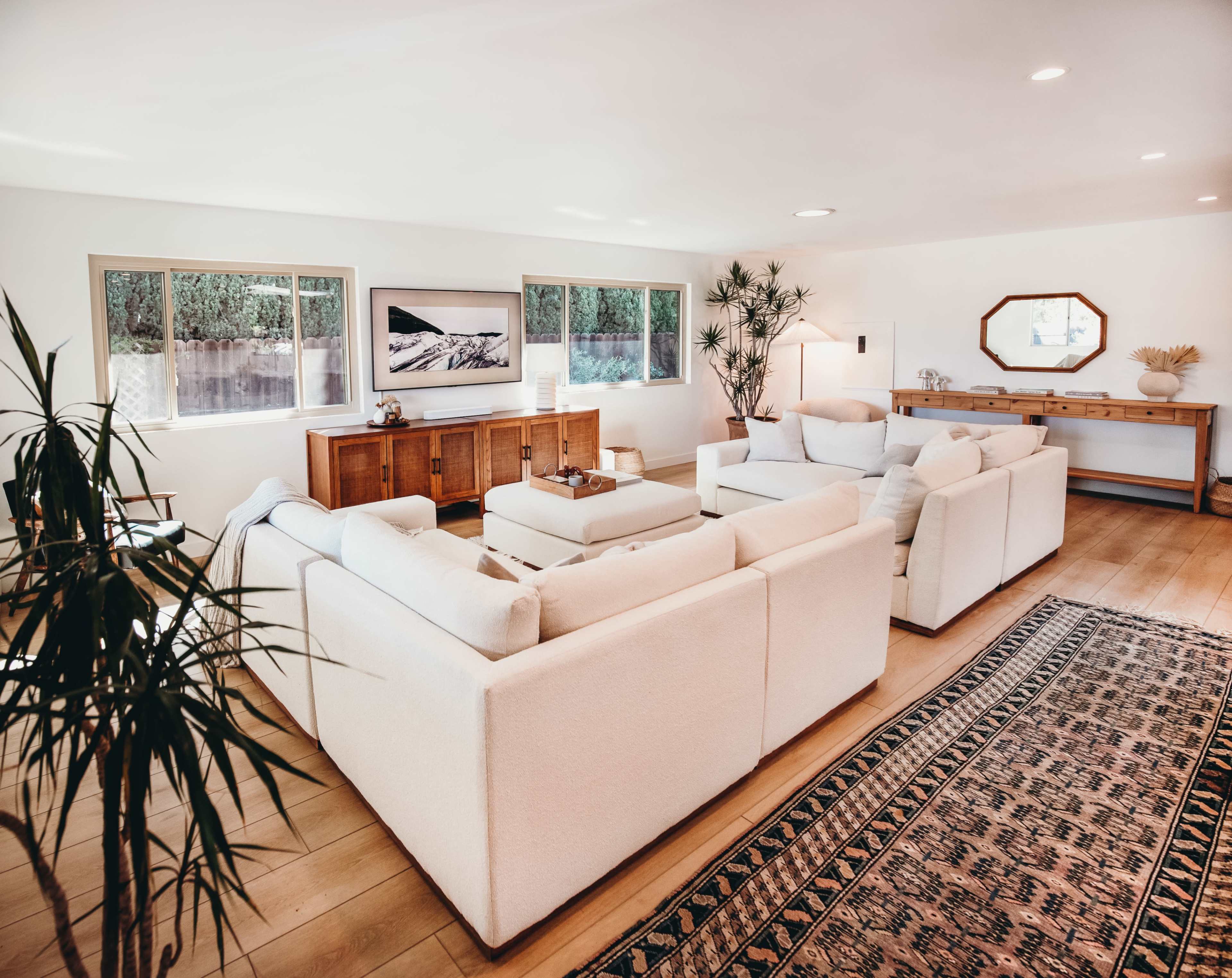 A spacious living room featuring a large sectional sofa, a wooden sideboard, and several windows allowing natural light to fill the space.