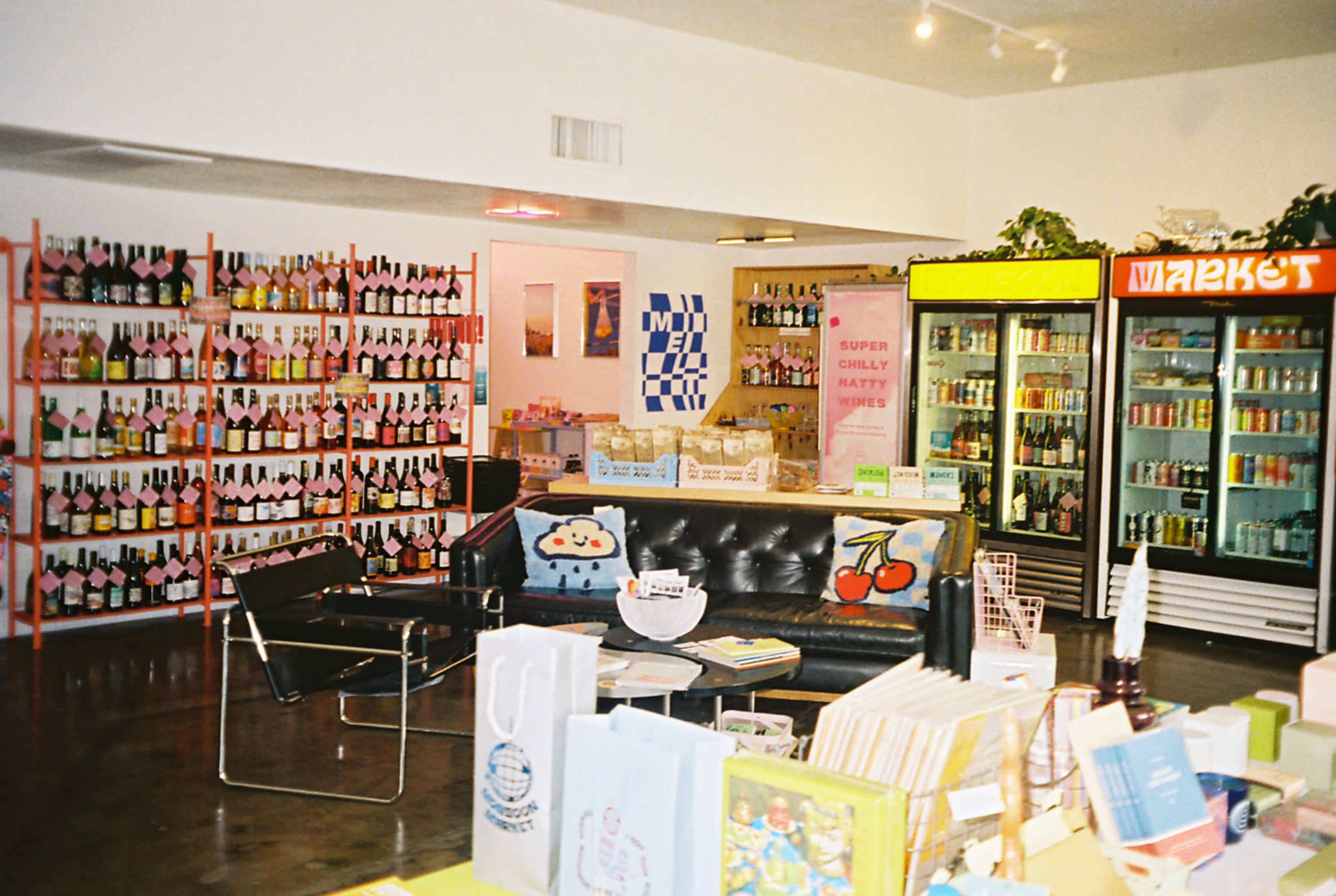 A brightly lit store interior featuring colorful shelves of beverages, a black seating area, and a display of books and bags on tables.