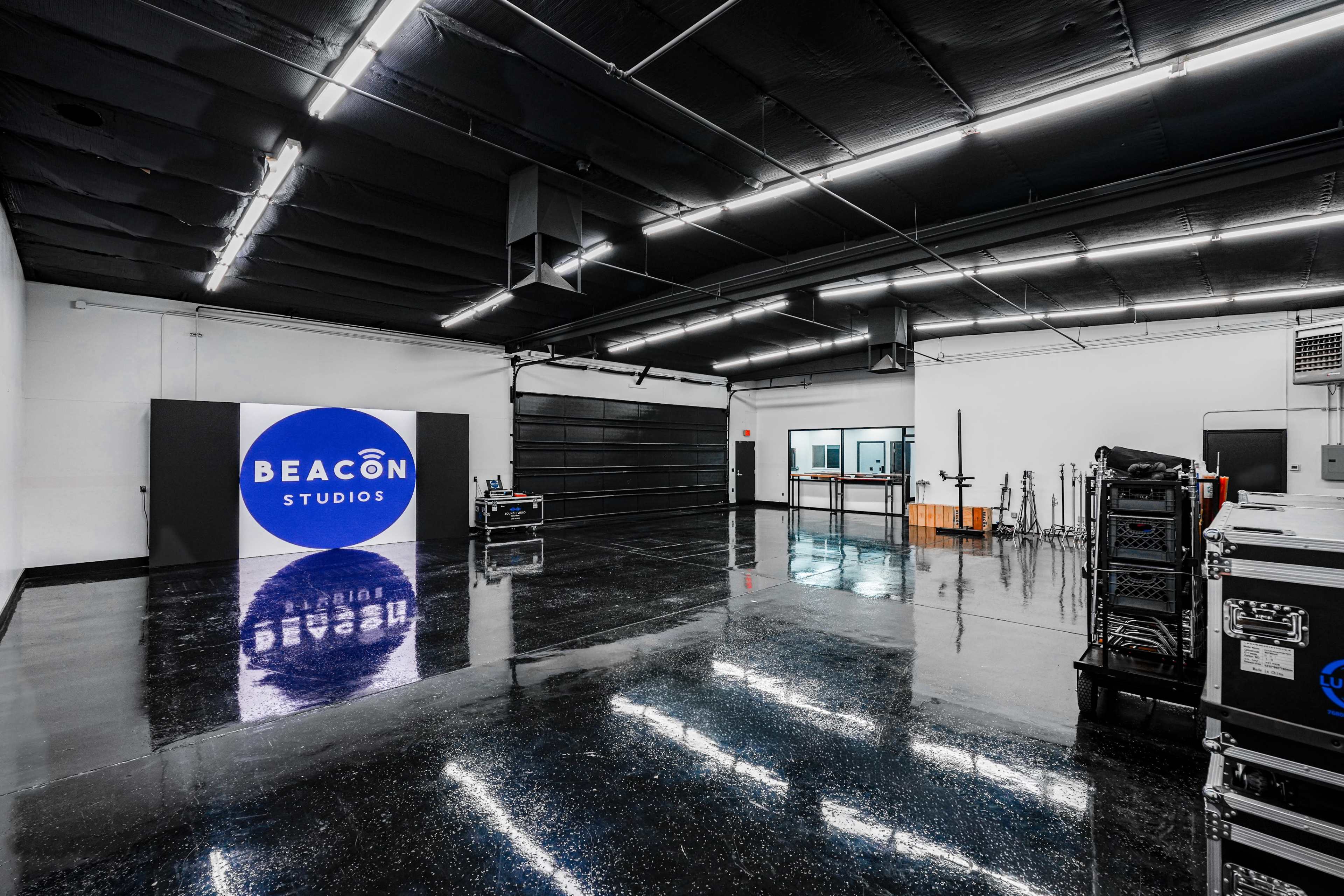 The image shows a spacious studio with a glossy black floor, featuring a sign that reads "BEACON STUDIOS" and equipment cases along the walls.