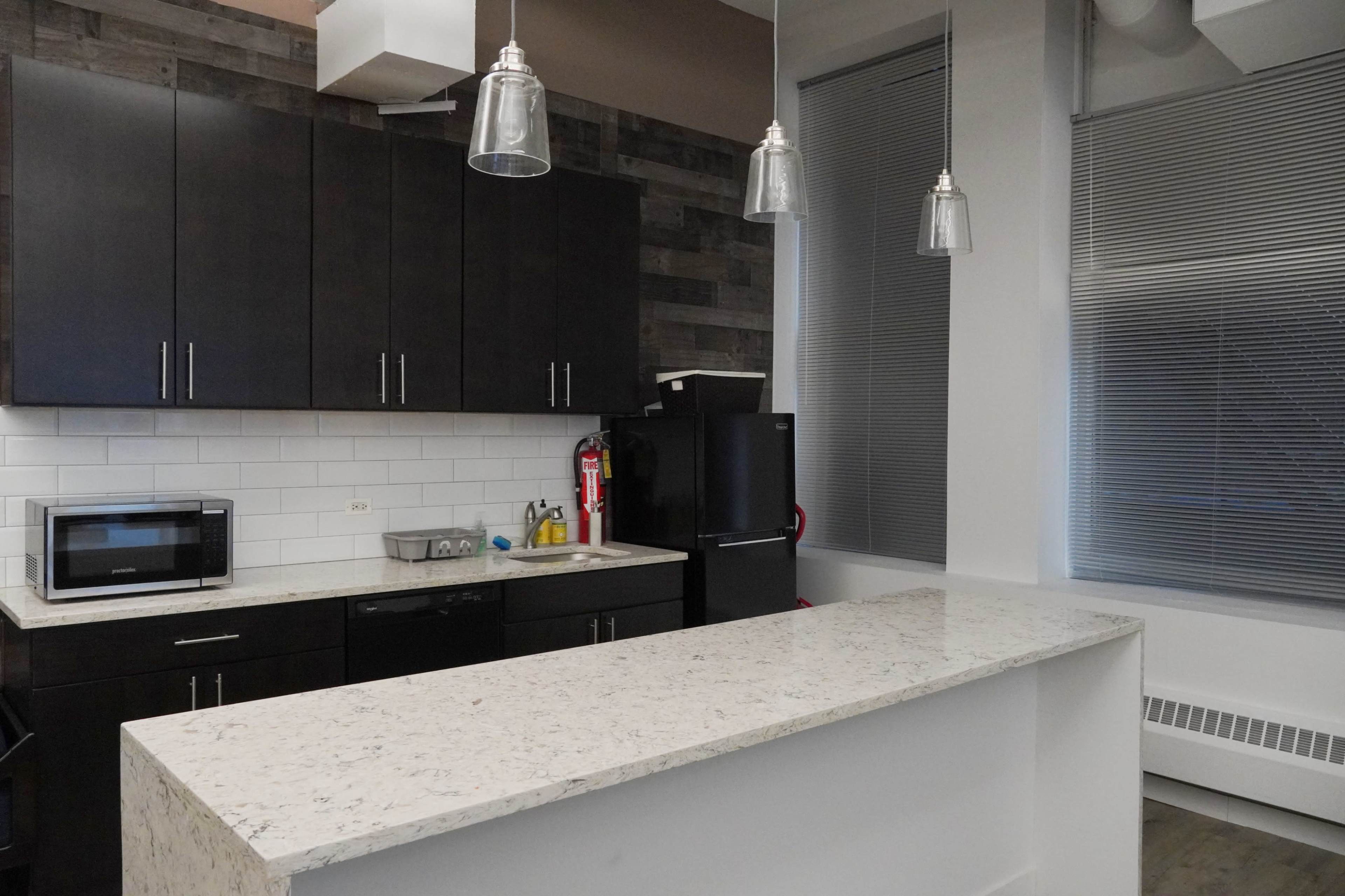 A modern kitchen featuring dark cabinetry, a white countertop, and stainless steel appliances.