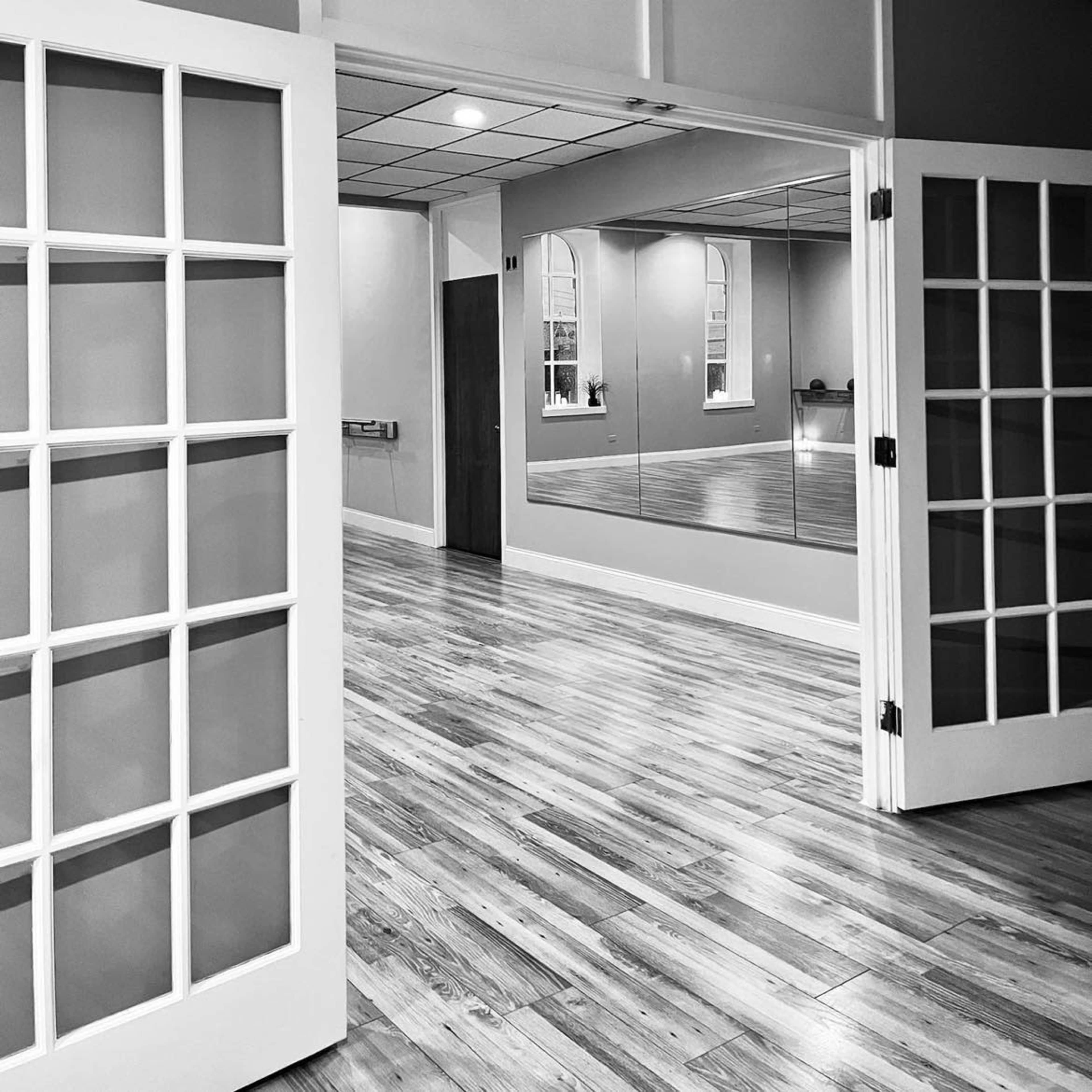 A dance studio features polished wooden floors, large mirrors, and double glass doors, creating an open space.