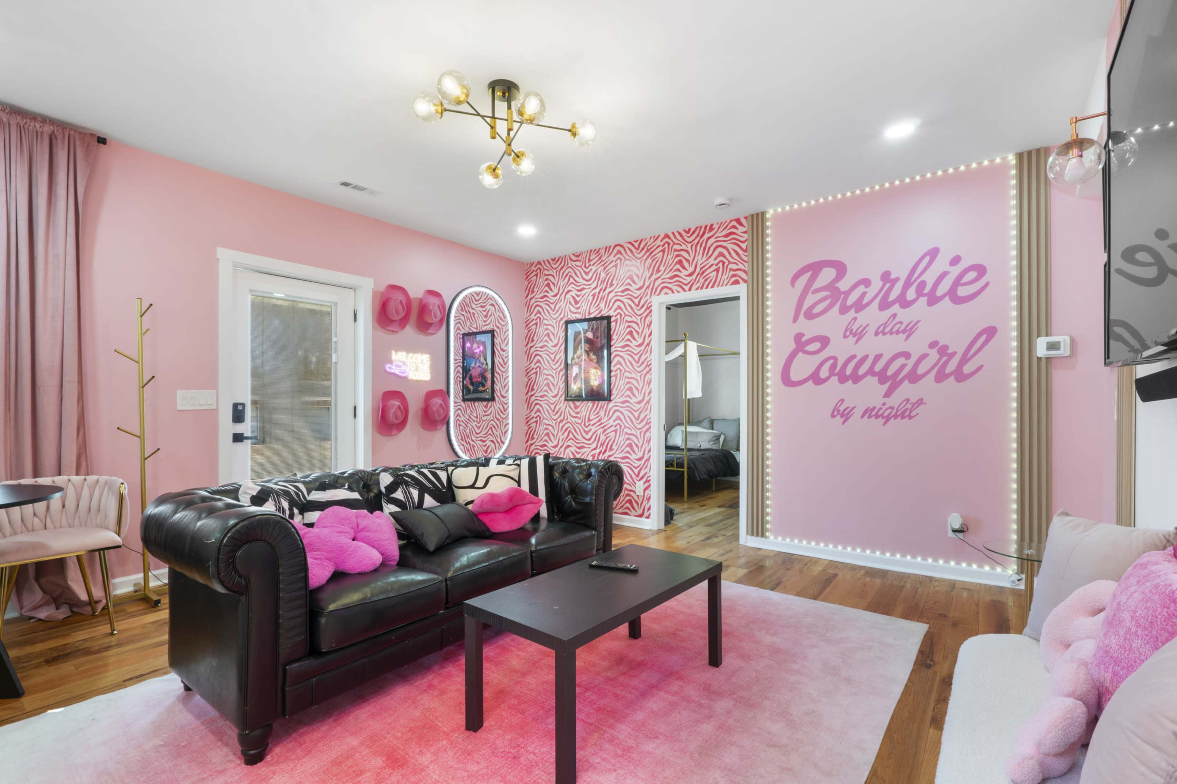 The living room features a black leather couch with pink pillows, a pink accent wall with the phrase "Barbie by day, Cowgirl by night," and a modern light fixture.