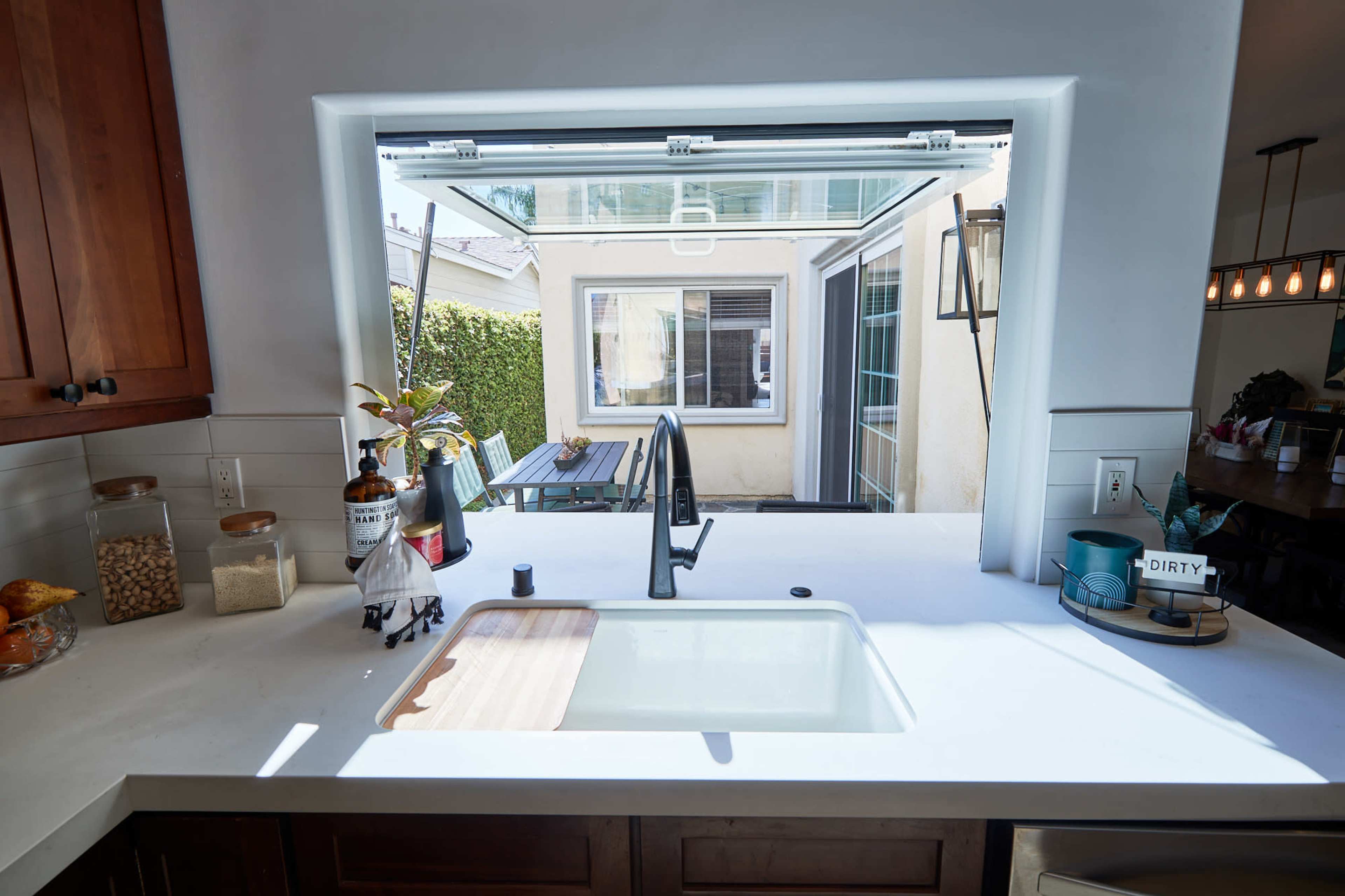 A kitchen with a sink and a window that opens to an outdoor patio area with a table.