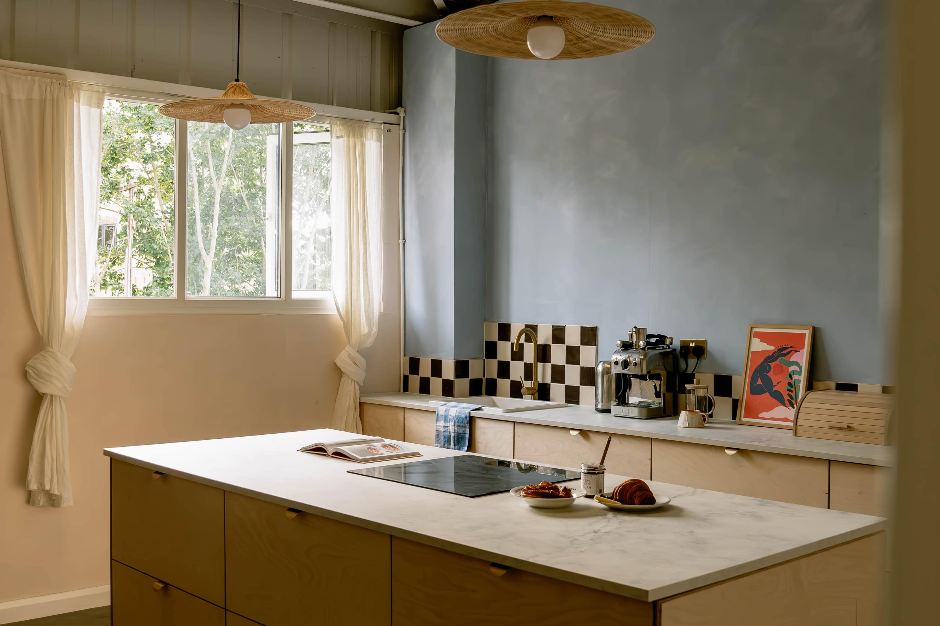 A modern kitchen features a large island with a marble countertop, a coffee machine, and a window overlooking greenery.
