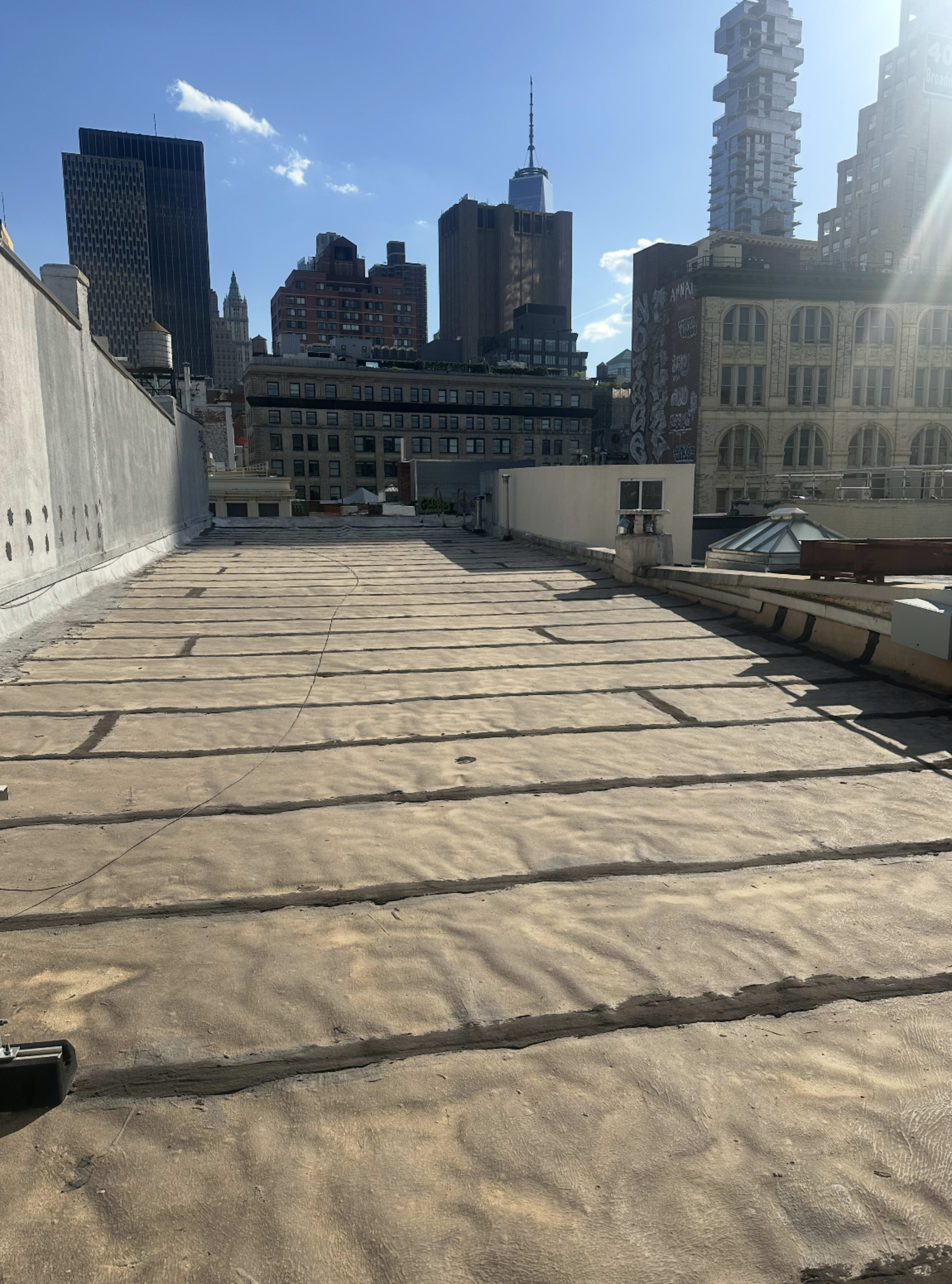The image shows a flat rooftop with visible seams, overlooking a city skyline that features a mix of modern and older buildings.