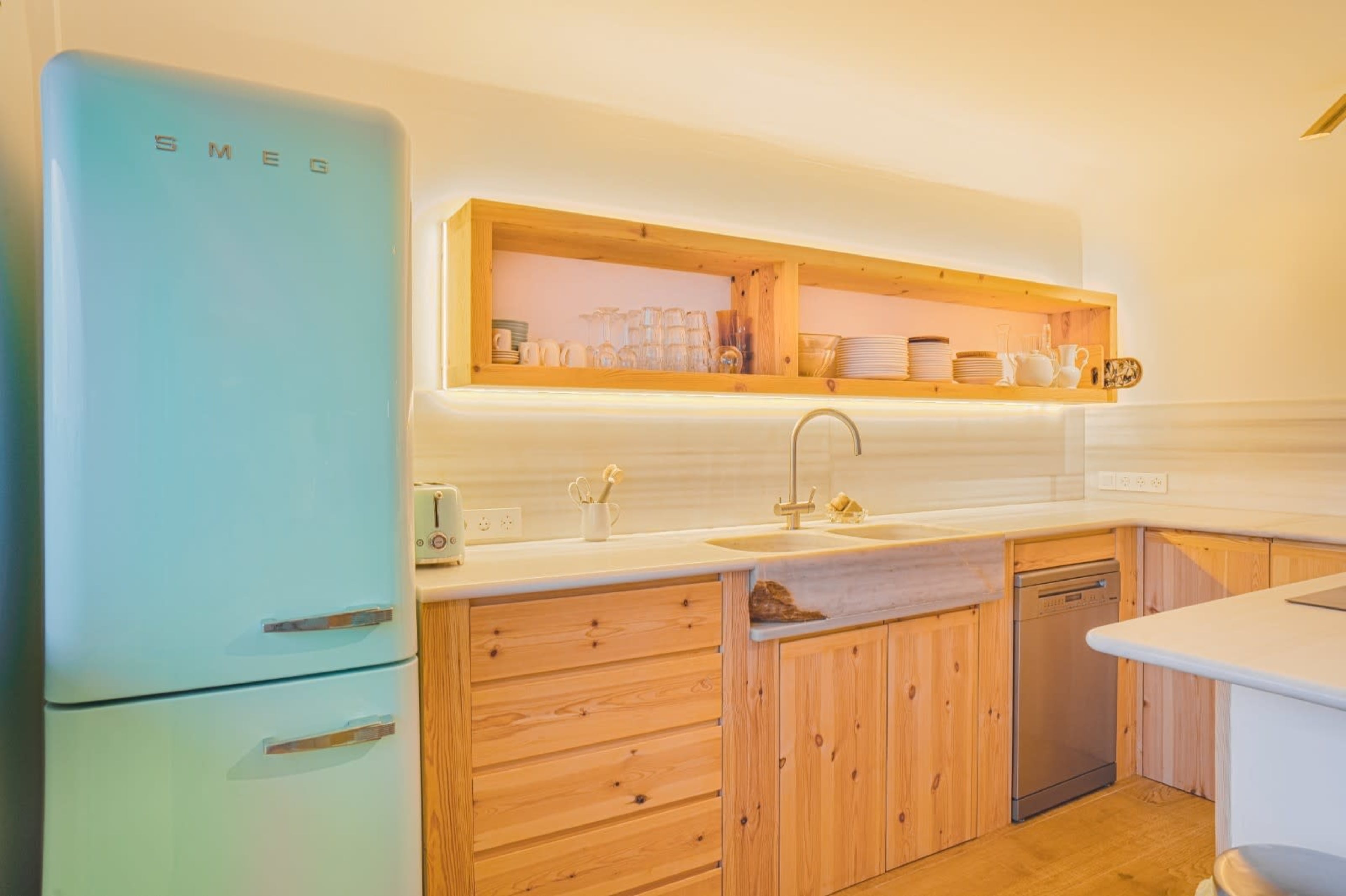 The image shows a modern kitchen featuring a retro-style light blue refrigerator, wooden cabinetry, and open shelves with dishware.