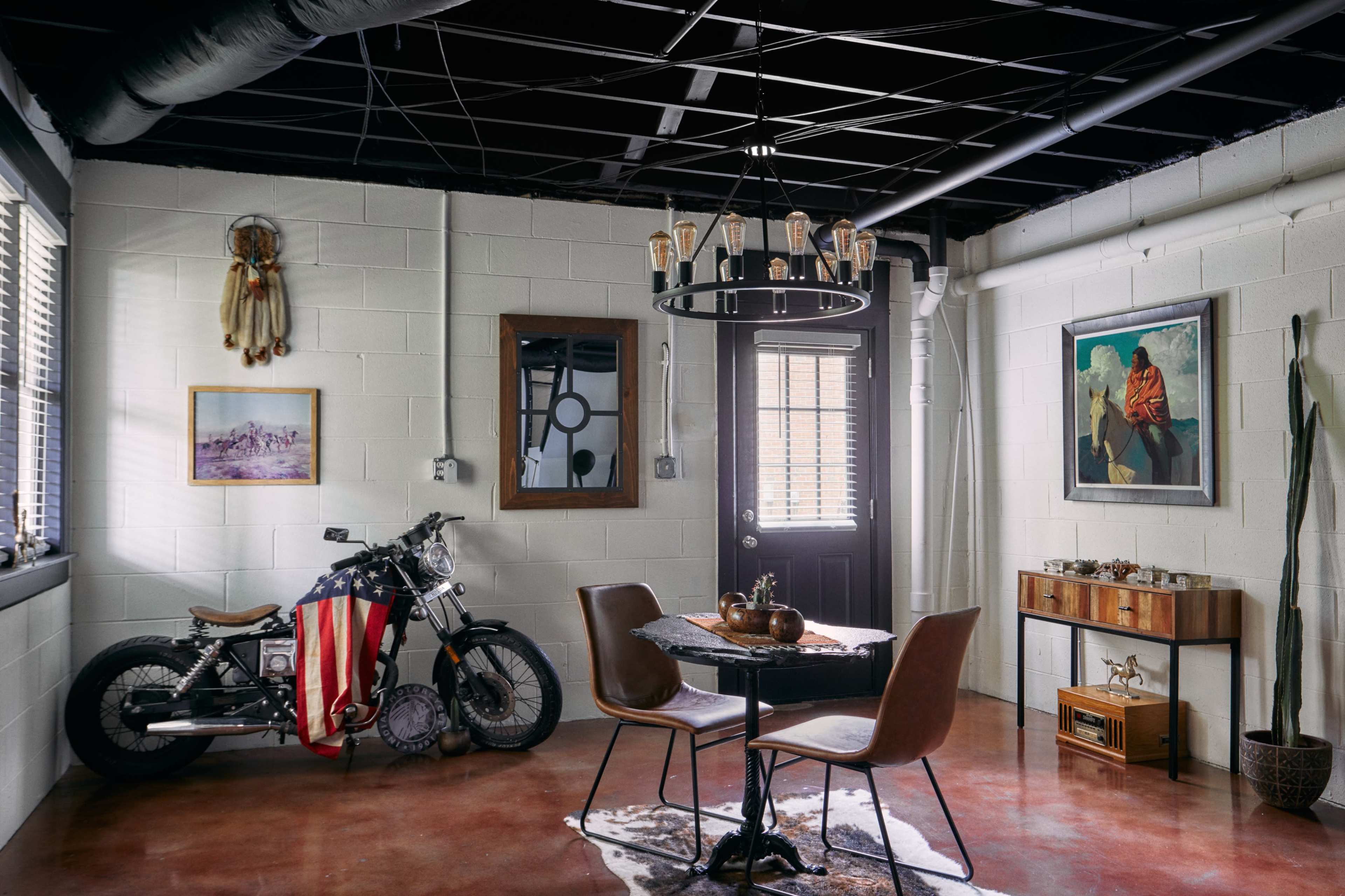 The room features a motorcycle draped with an American flag, a round dining table with chairs, and various wall decorations including artwork and a mirror.