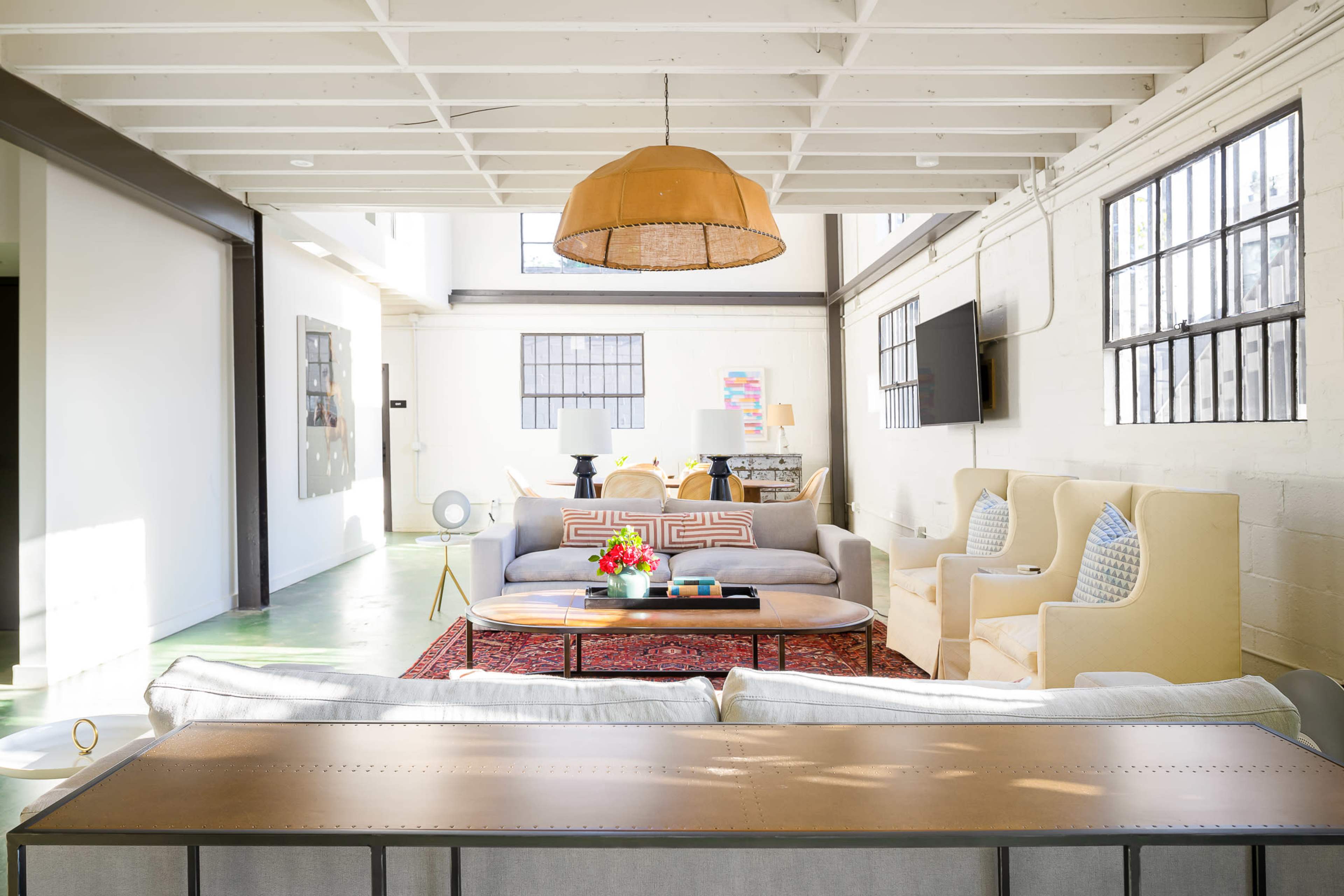 A spacious living area with a light-colored sofa, a coffee table with flowers, and warm lighting from a pendant lamp, arranged around a decorative rug.