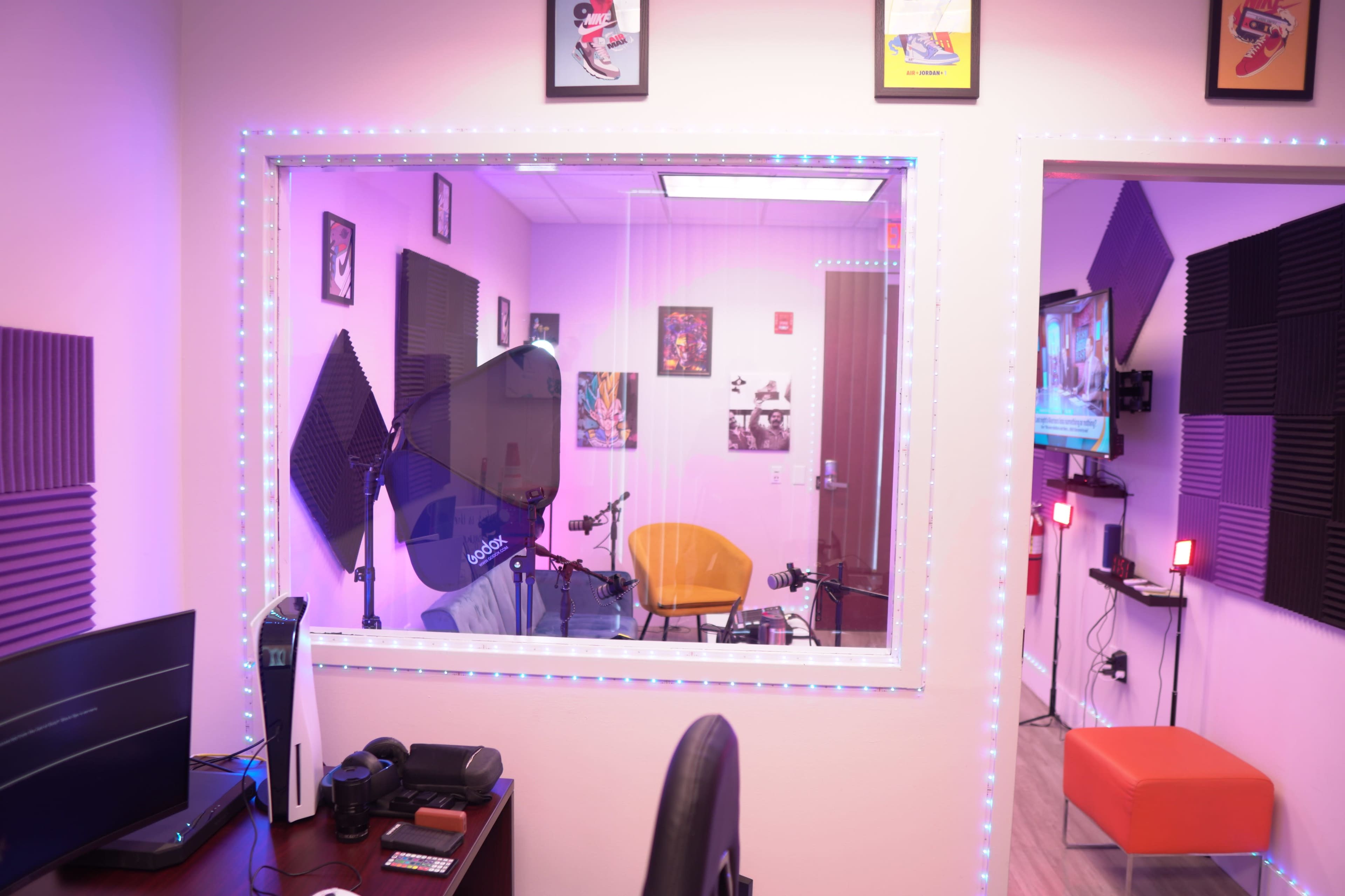 A brightly lit recording studio featuring a large window, colorful decorations, and multiple microphones set up around a central chair.