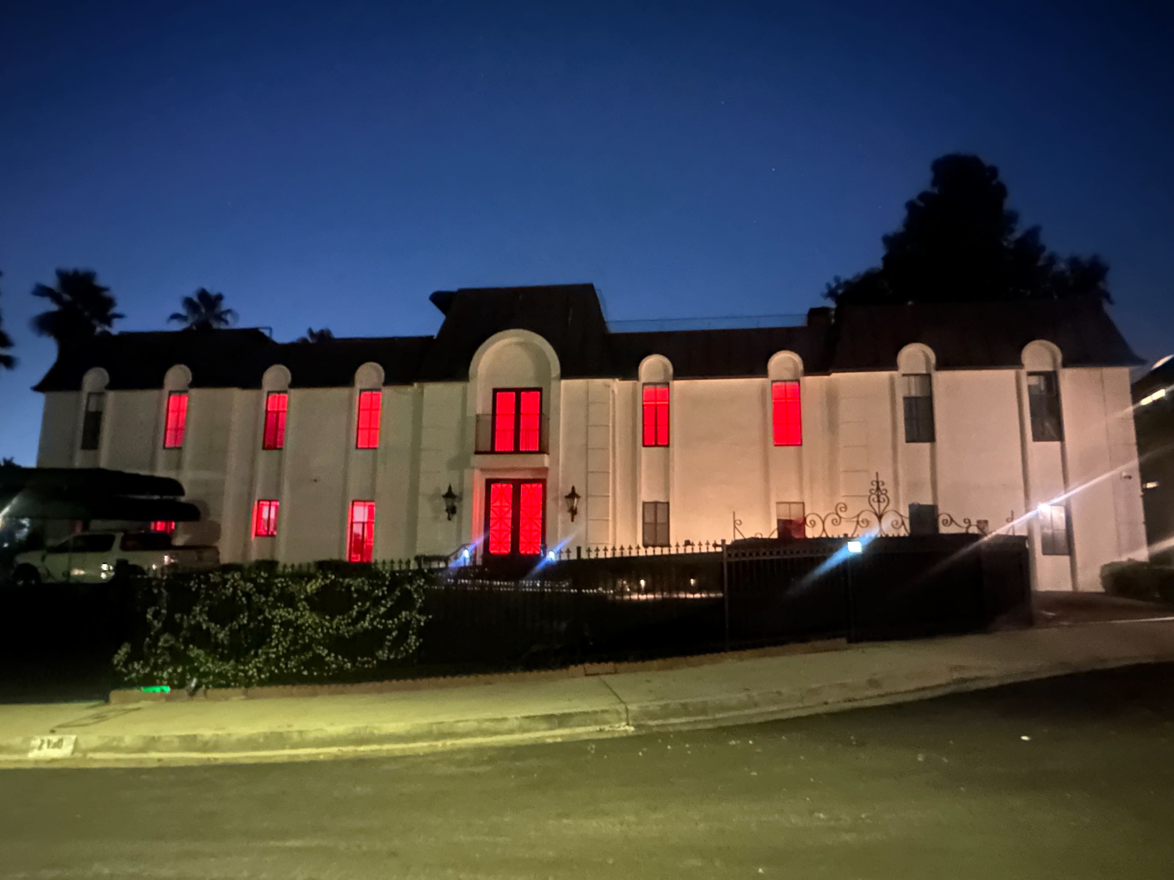 A large house with red-lit windows is located on a quiet street during twilight.