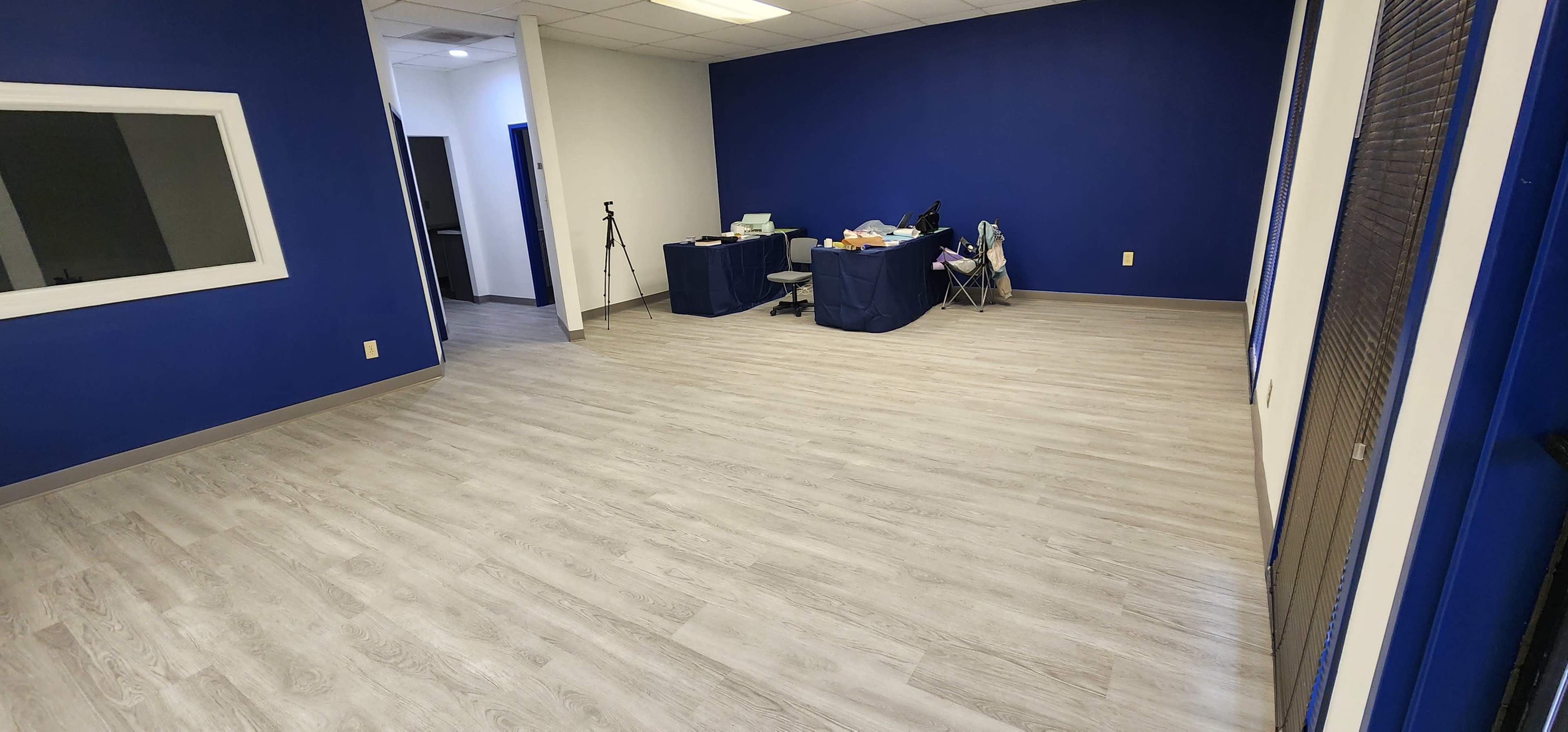 The image shows a spacious room with light gray flooring, blue walls, and a table covered with items at the far end.