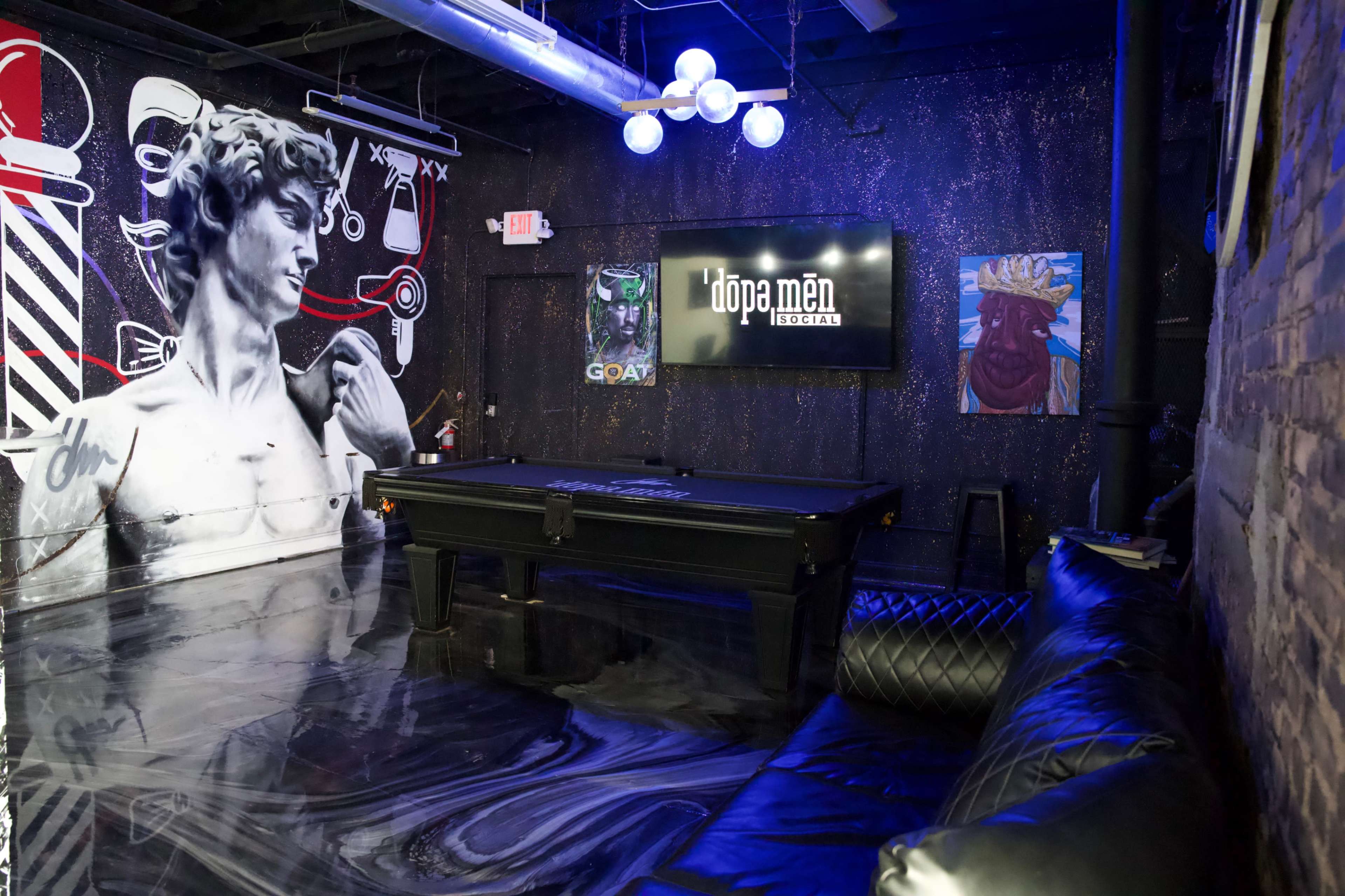 The image shows a stylish room with a pool table, a leather couch, colorful wall art including a depiction of David, and modern lighting fixtures.