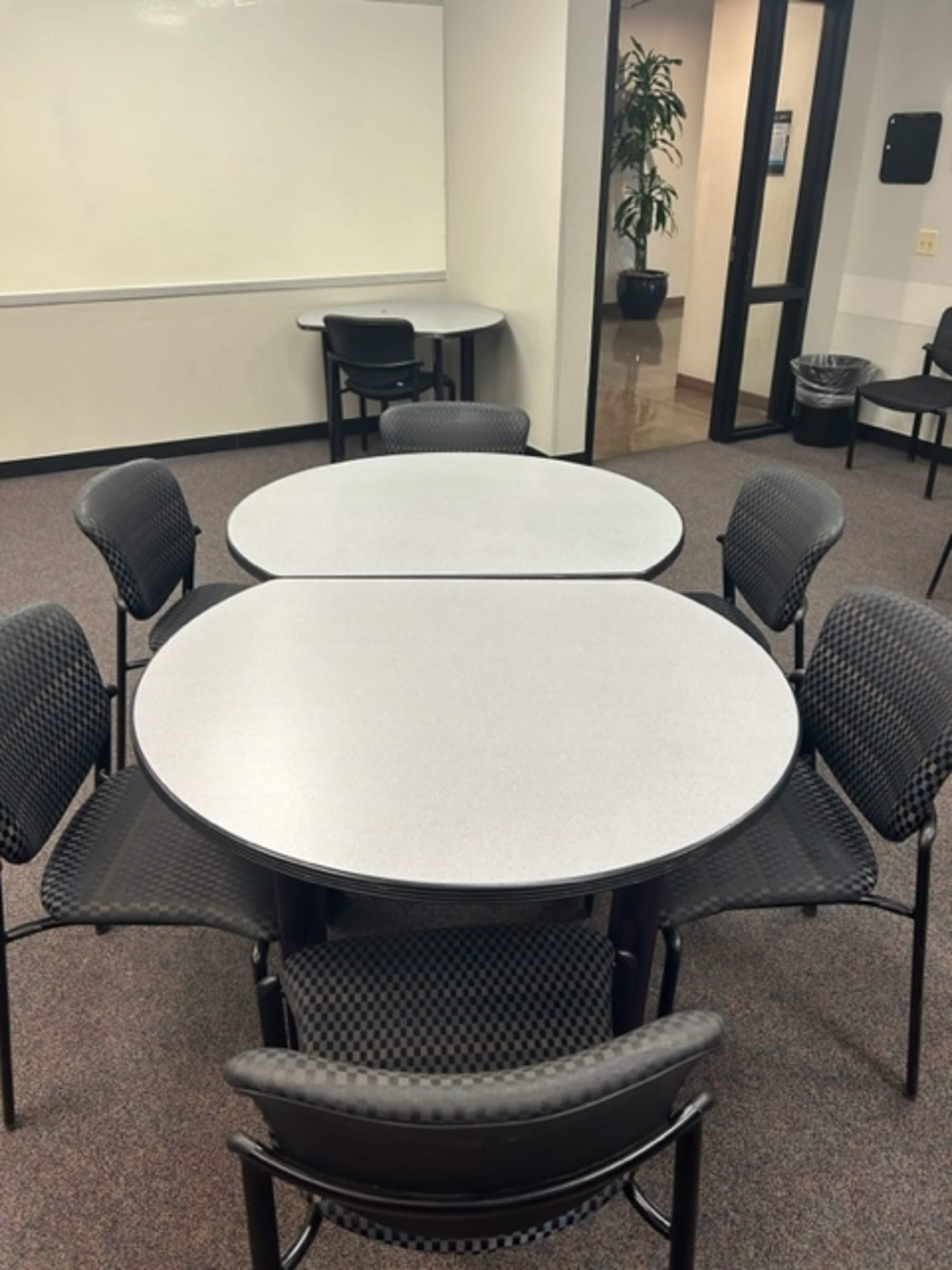 Two gray tables arranged in an empty room with black chairs around them.