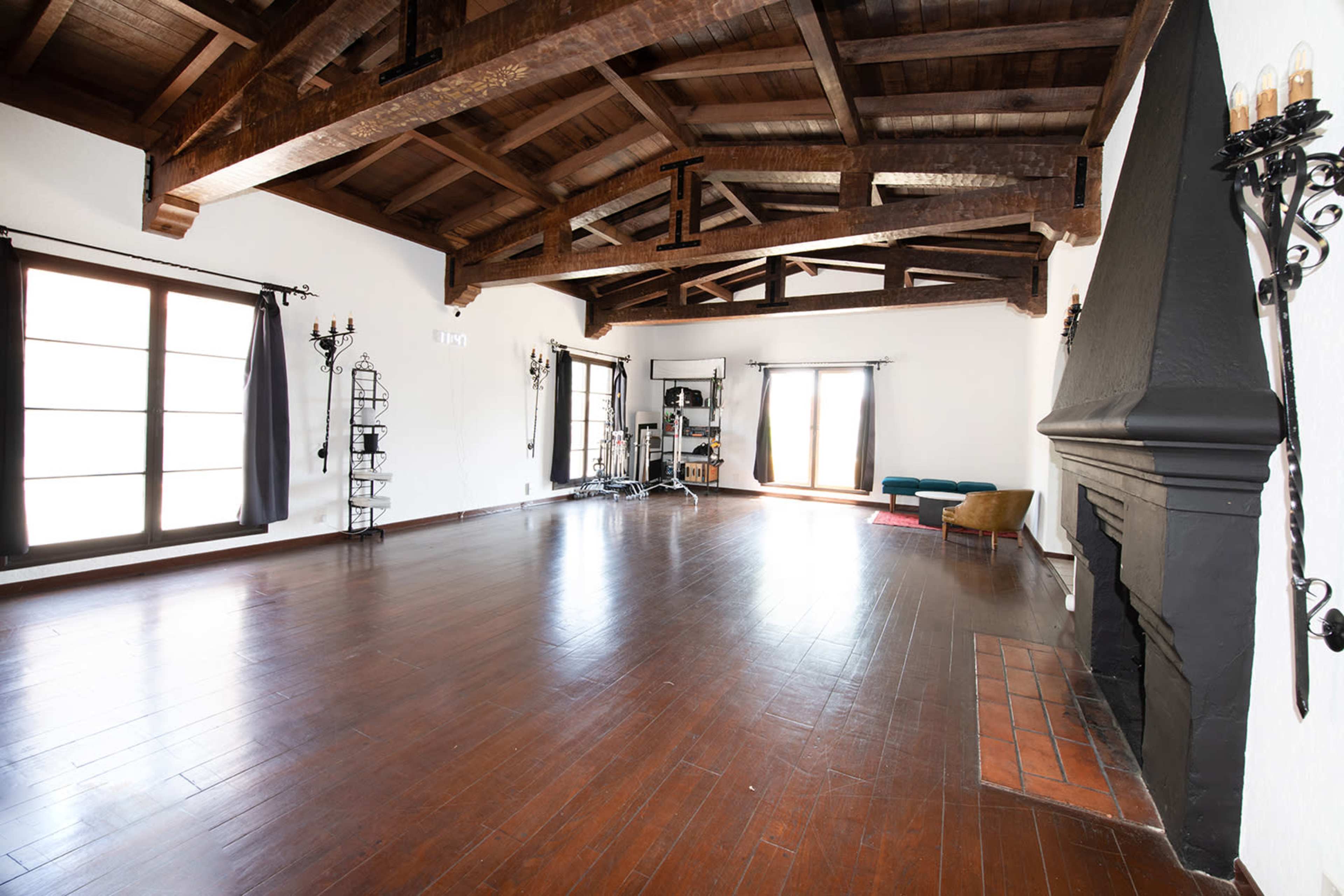 A spacious room with wooden beams, large windows, and a fireplace, featuring minimal furniture and an open layout.