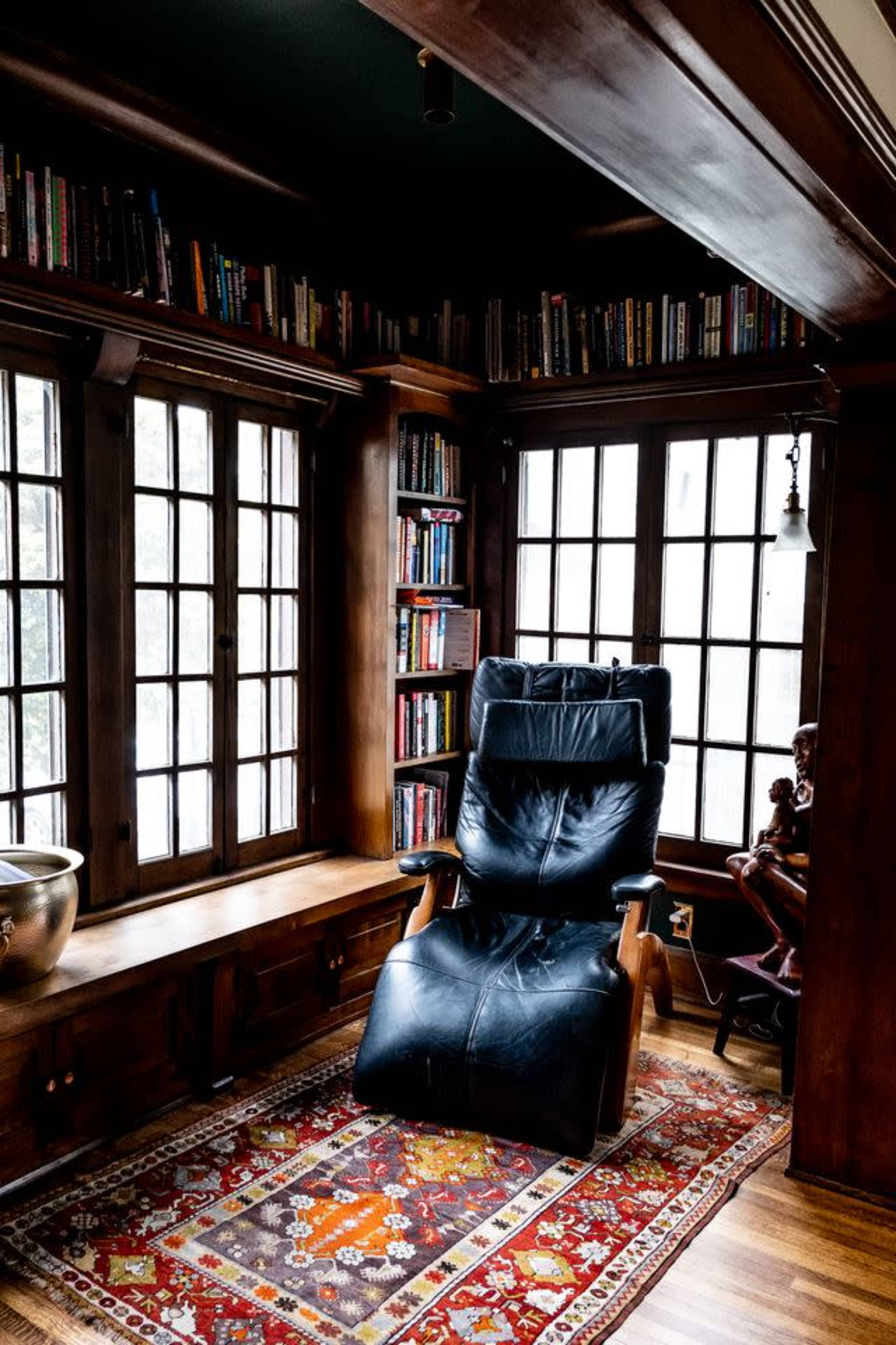 A black leather recliner sits in a cozy nook surrounded by tall windows and shelves filled with books.