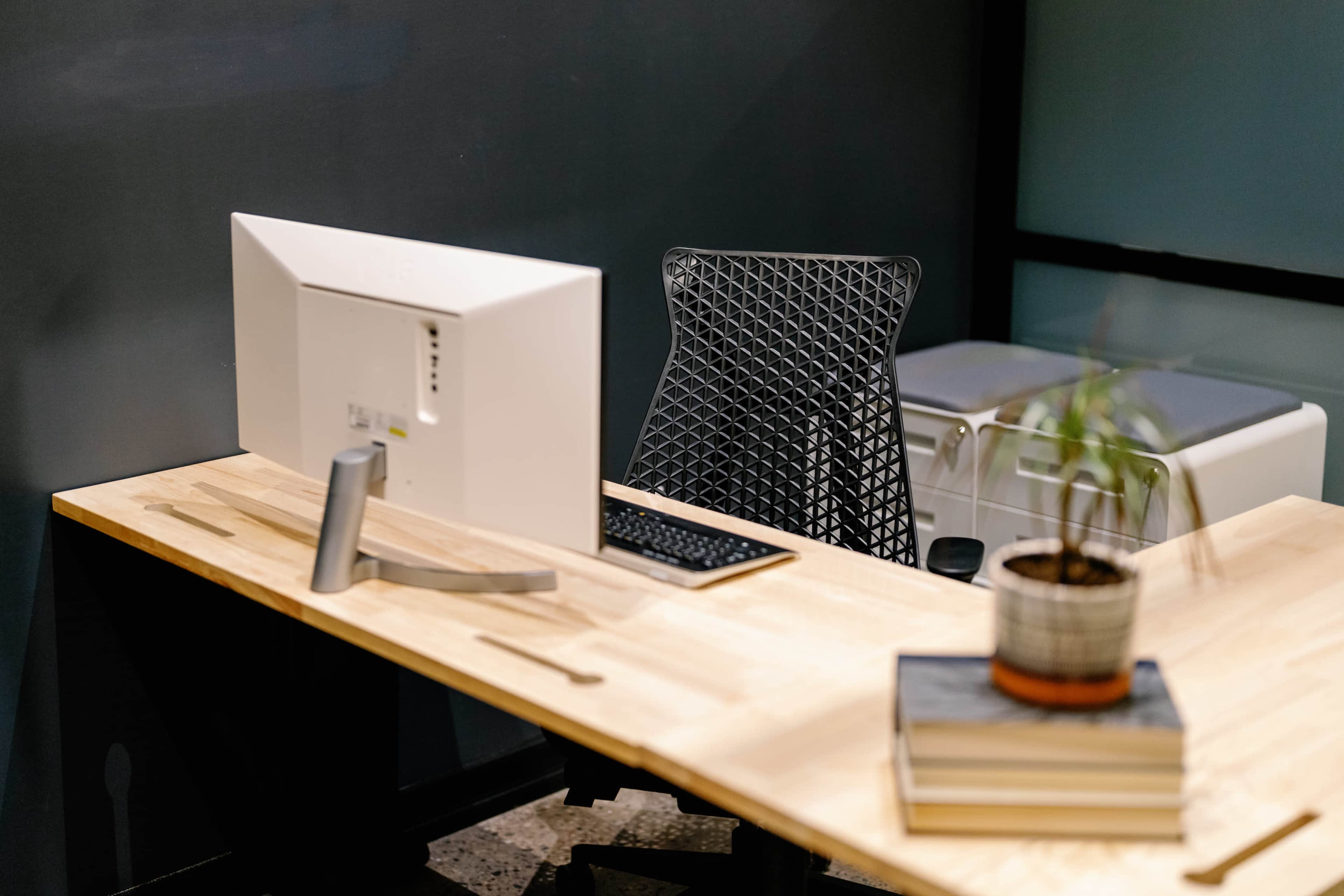 A modern desk with a computer monitor and keyboard, accompanied by a small potted plant and stacked books.