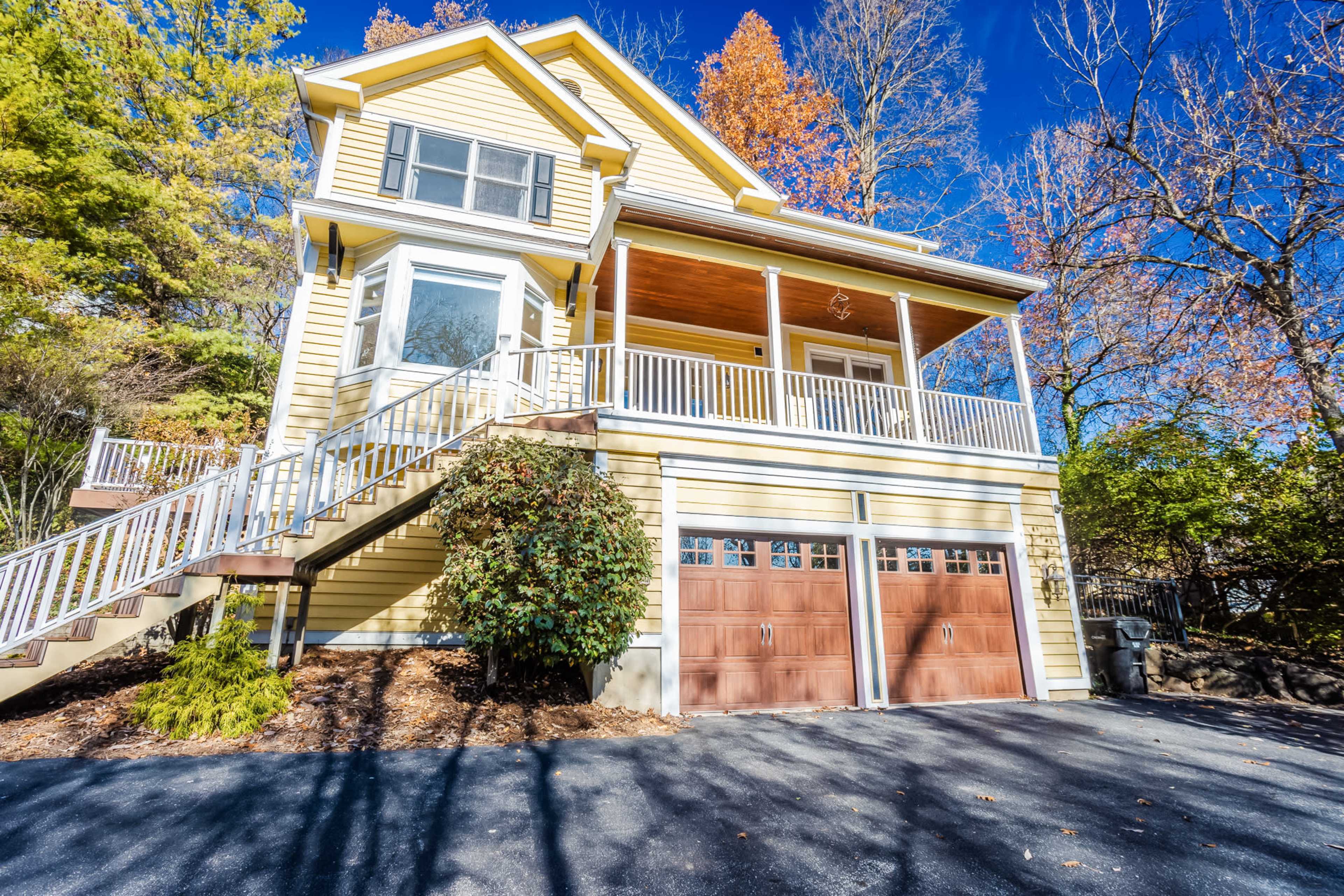 A yellow two-story house with a large front porch and a driveway featuring a two-car garage.