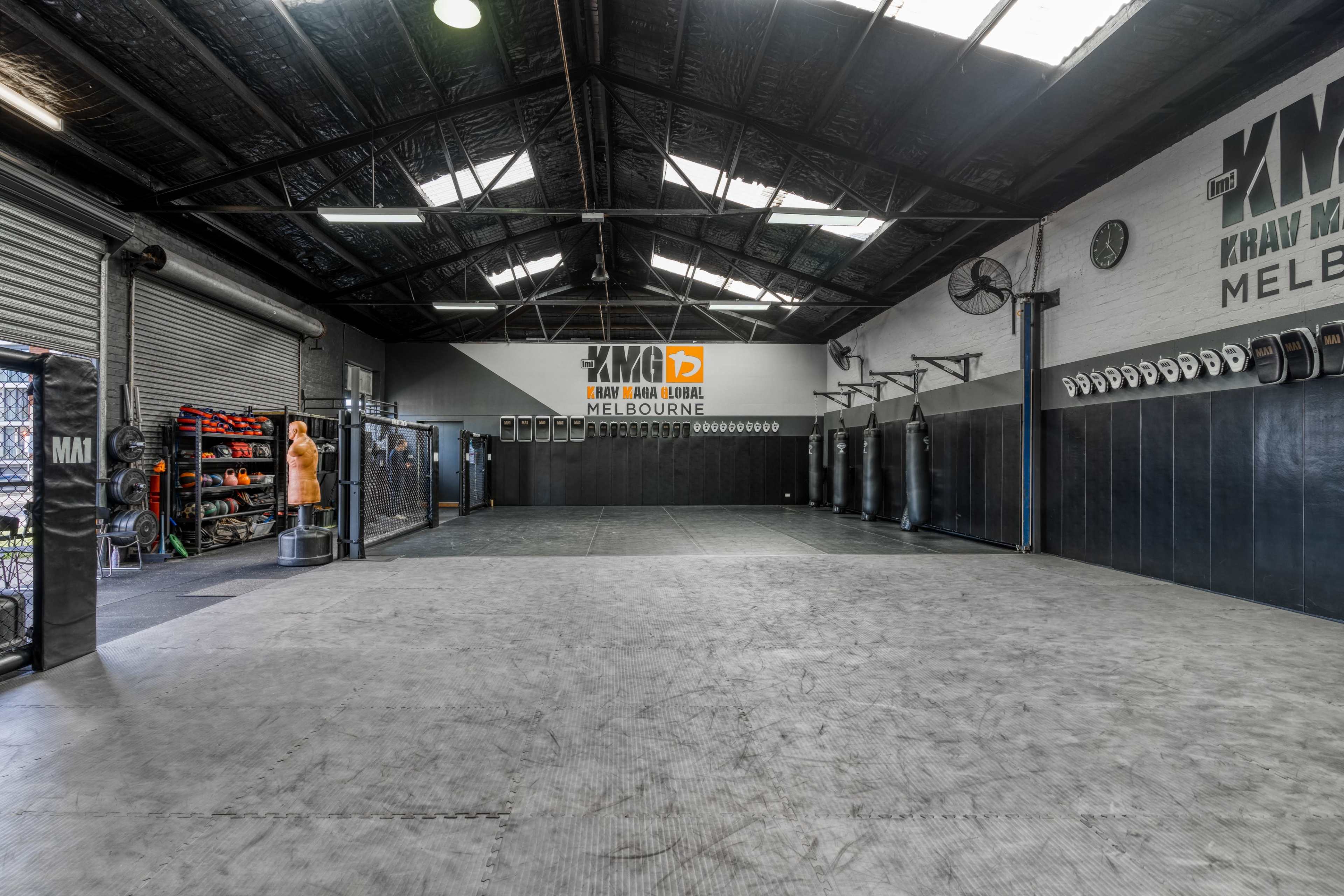 An empty martial arts training facility with punching bags and fitness equipment along the walls.