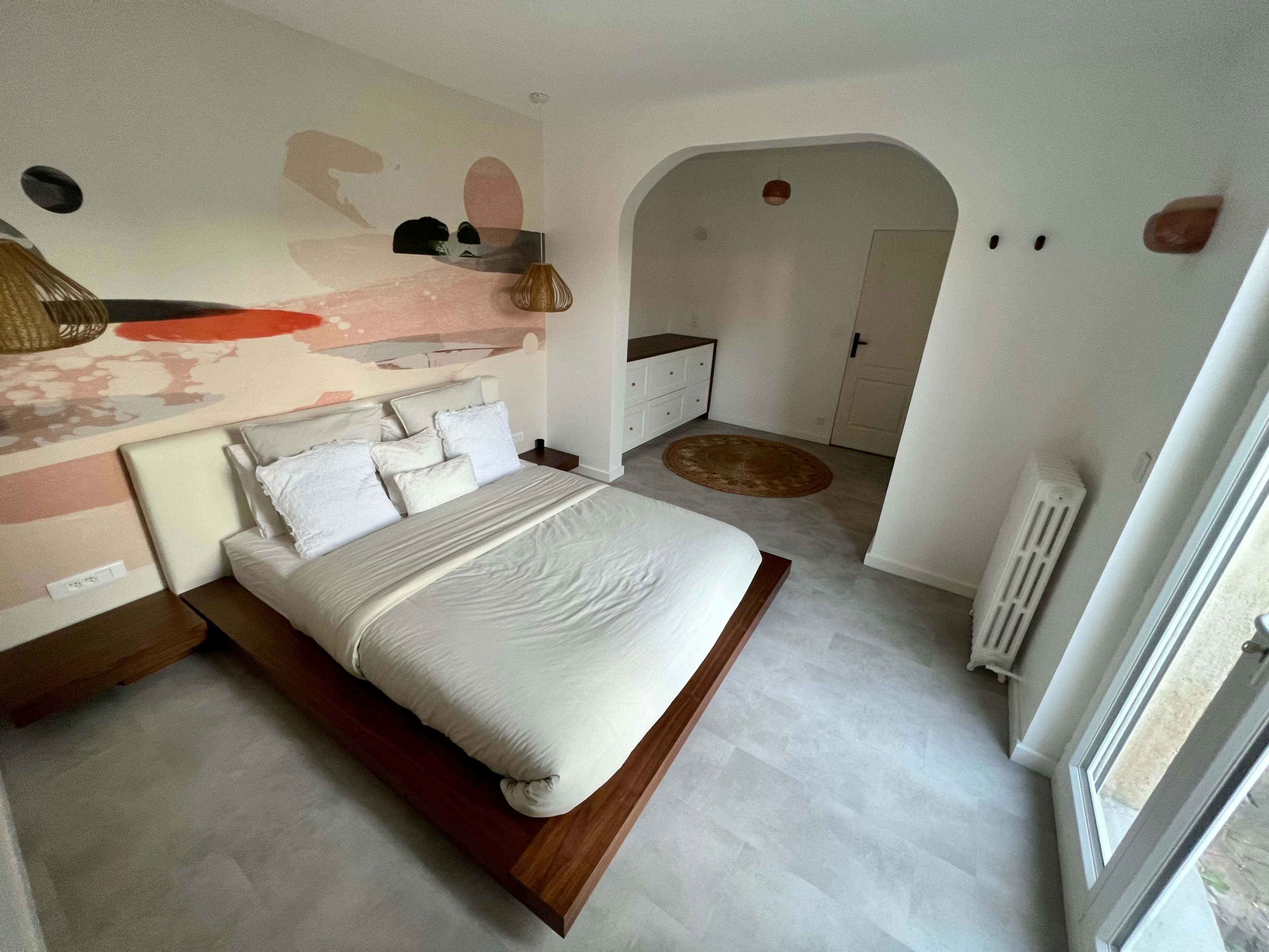A minimalist bedroom with a bed, a dresser, and light-colored walls featuring abstract designs.