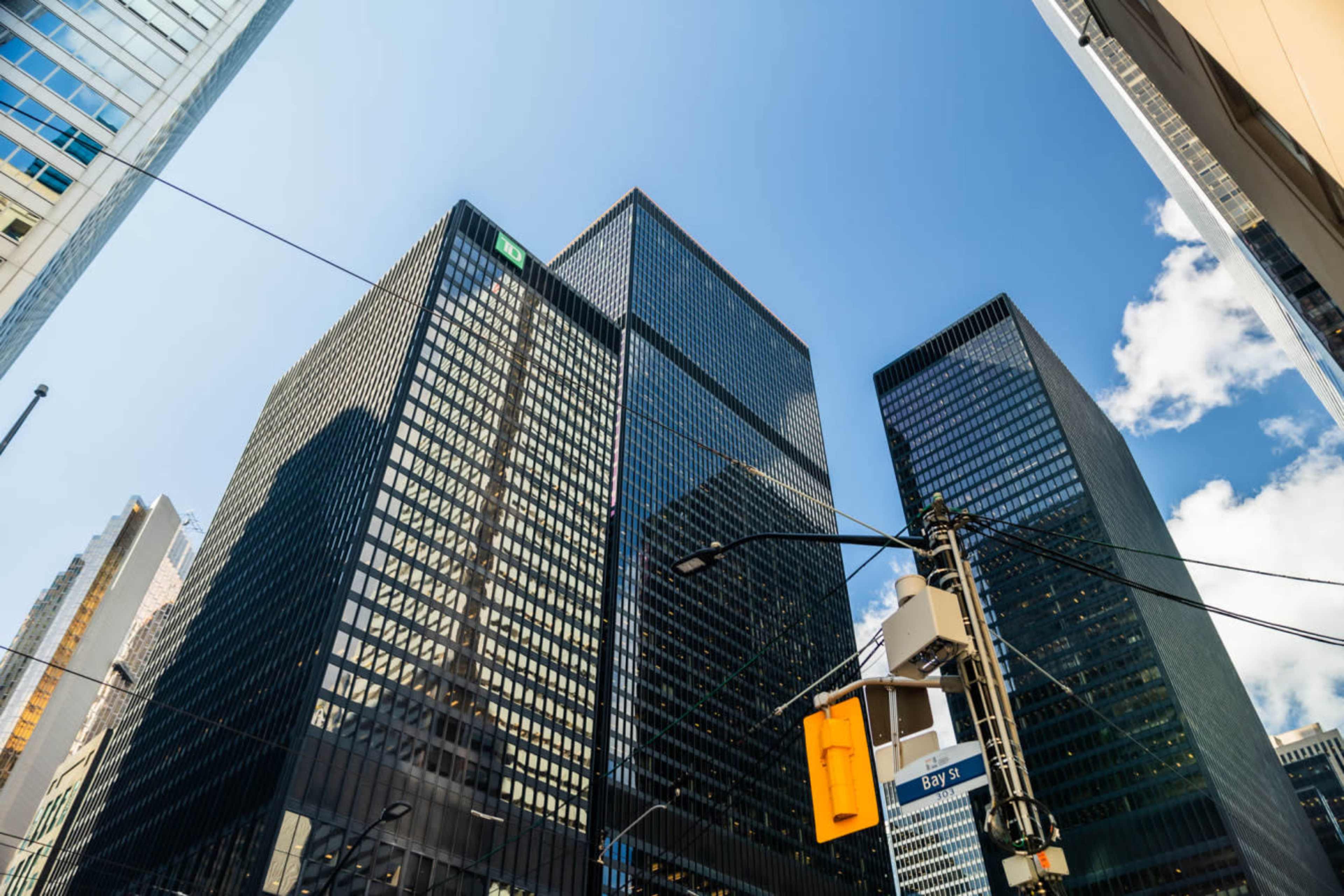 A view of tall glass skyscrapers against a blue sky with clouds, viewed from street level.