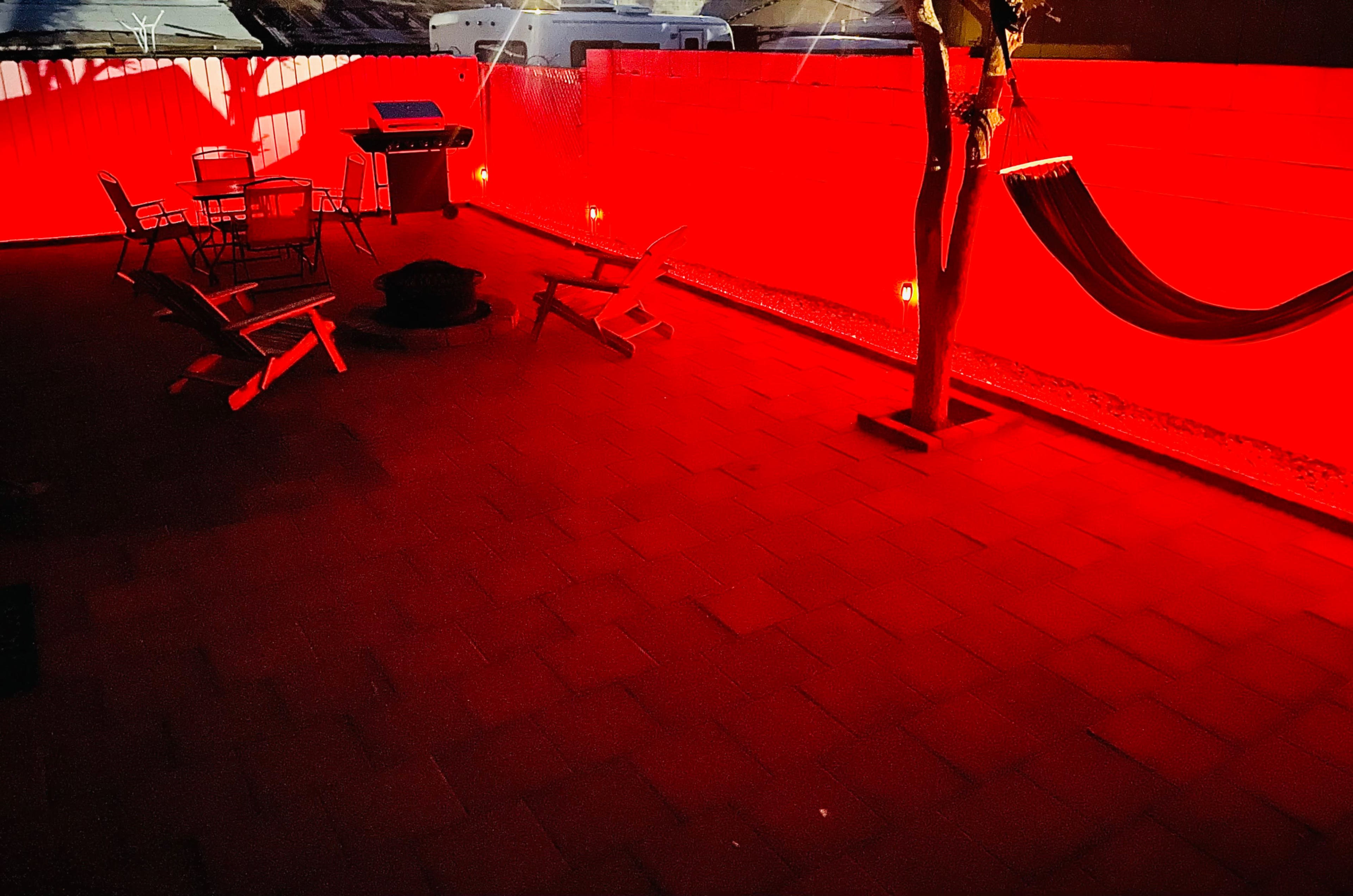 A patio area features a grill, seating, and a hammock, all illuminated by red lights against a contrasting wall.
