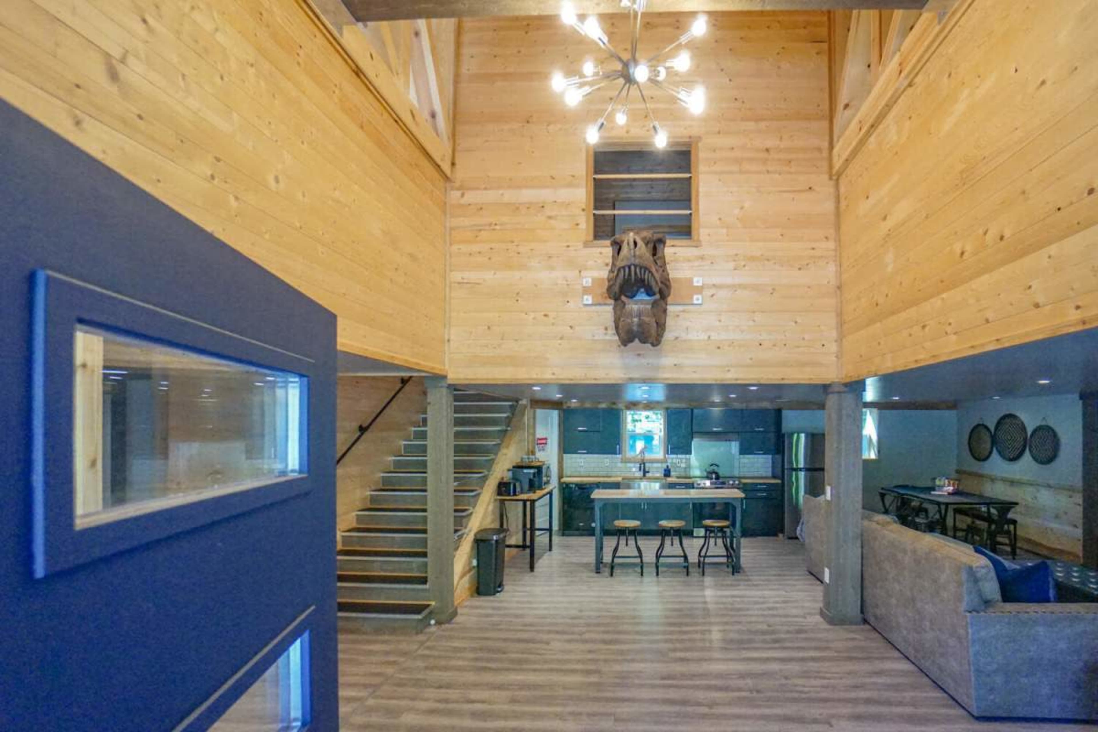 A modern, wooden interior of a home with high ceilings, featuring a staircase, a kitchen area, and a decorative mounted animal head.