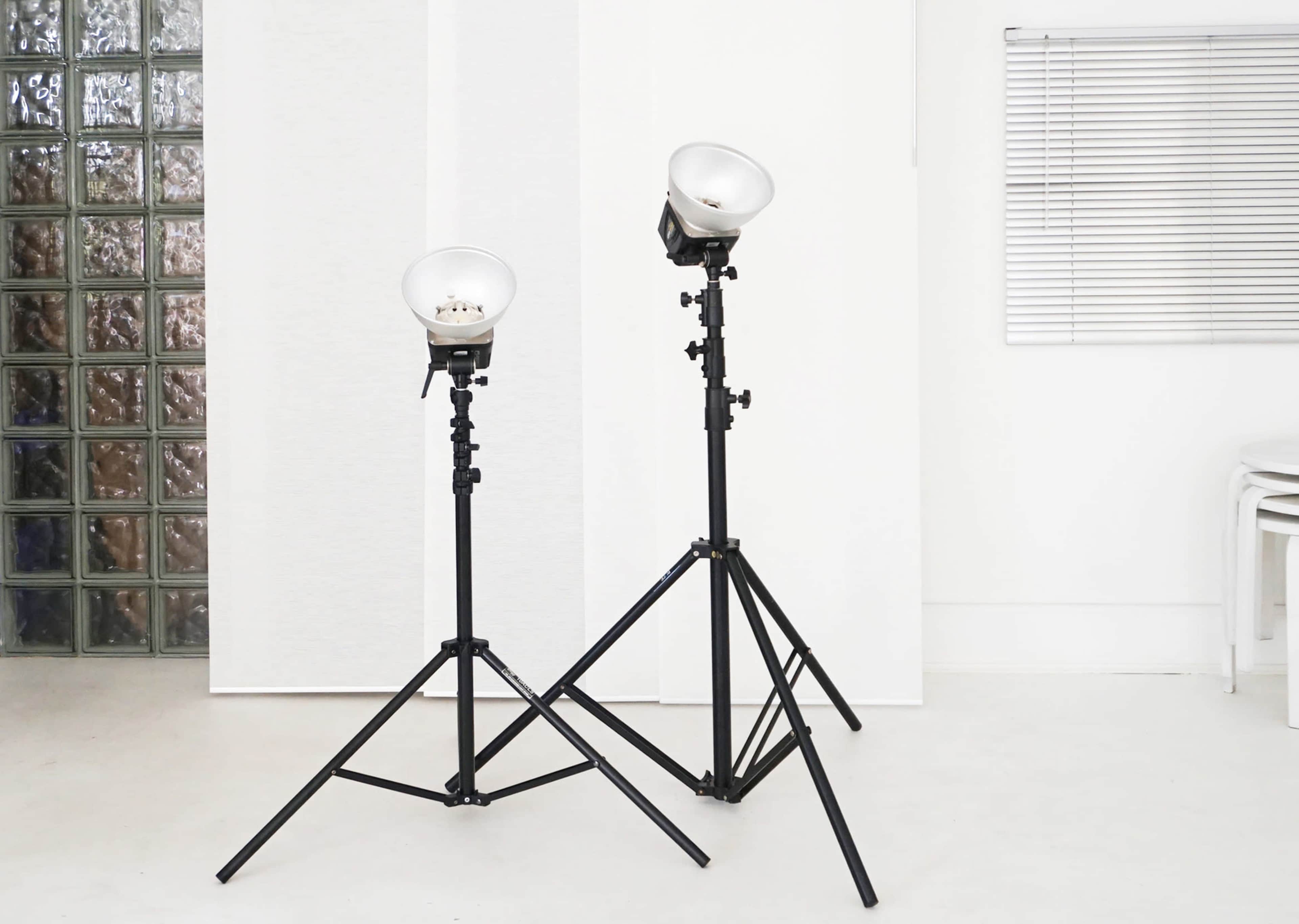 Two photography lights on black tripods stand in a bright, minimalistic studio space.