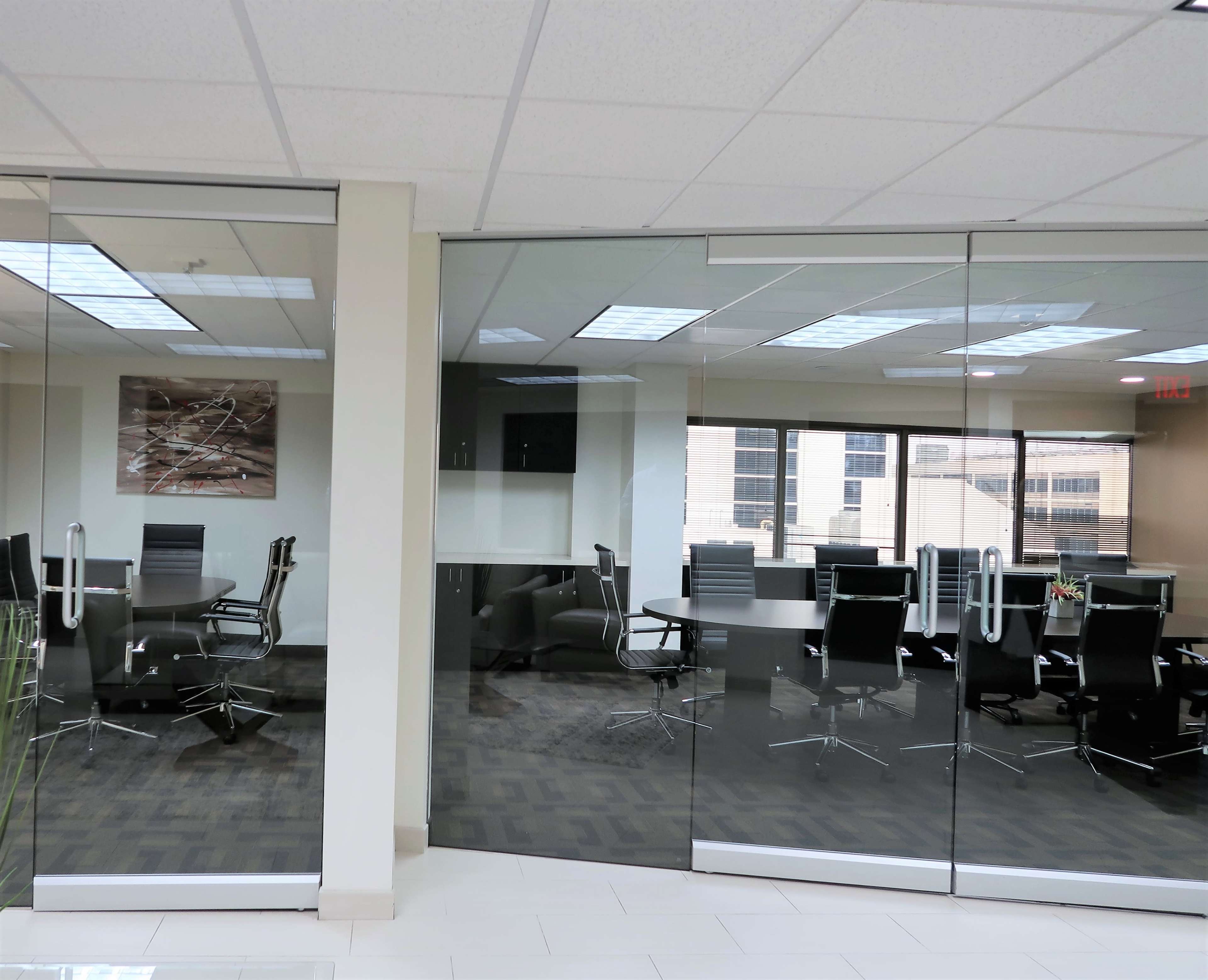 A modern office space with glass walls, featuring a conference room with black chairs and a large table.