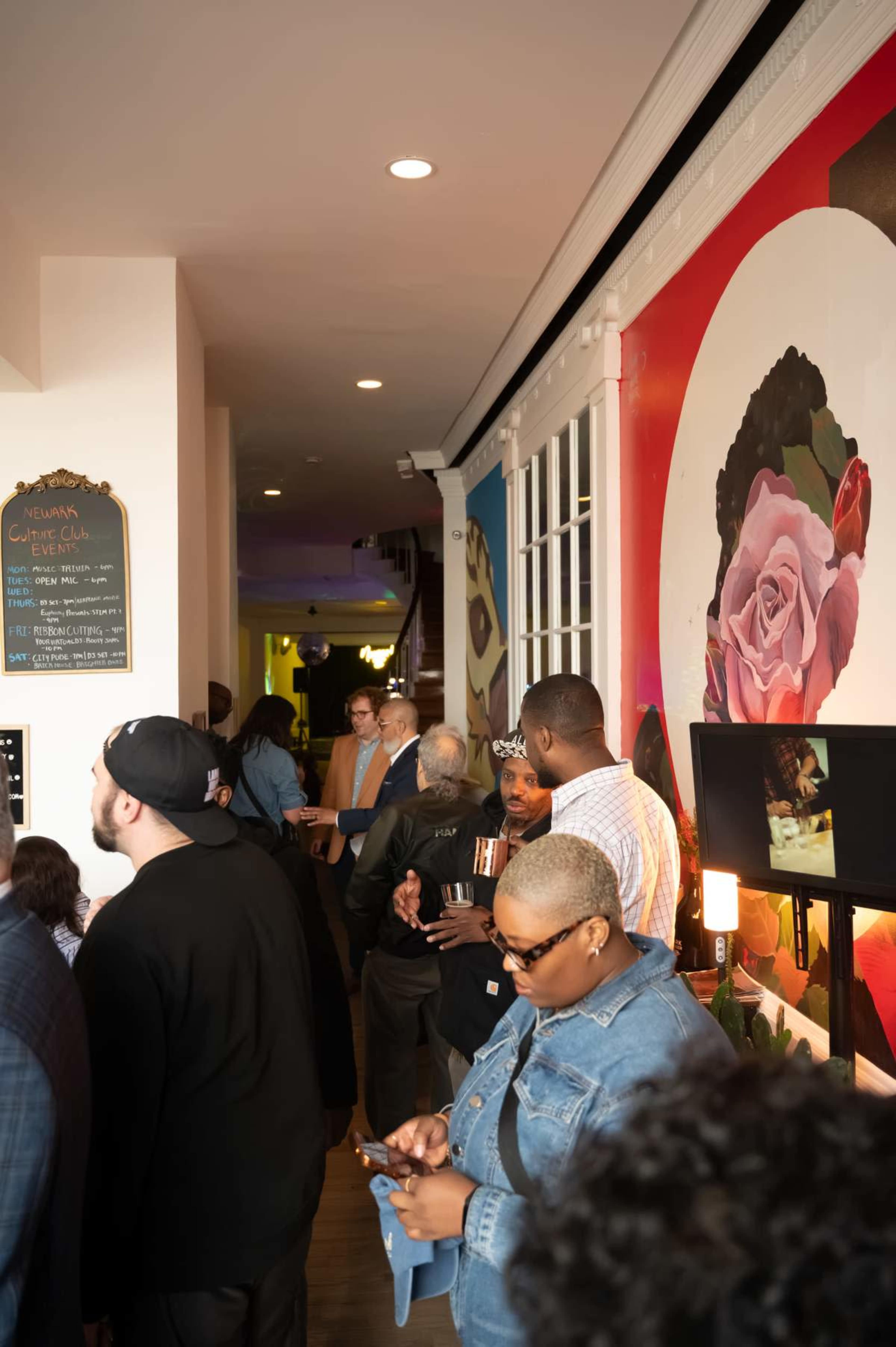 A group of people stands in a narrow hallway lined with colorful artwork and a chalkboard menu.