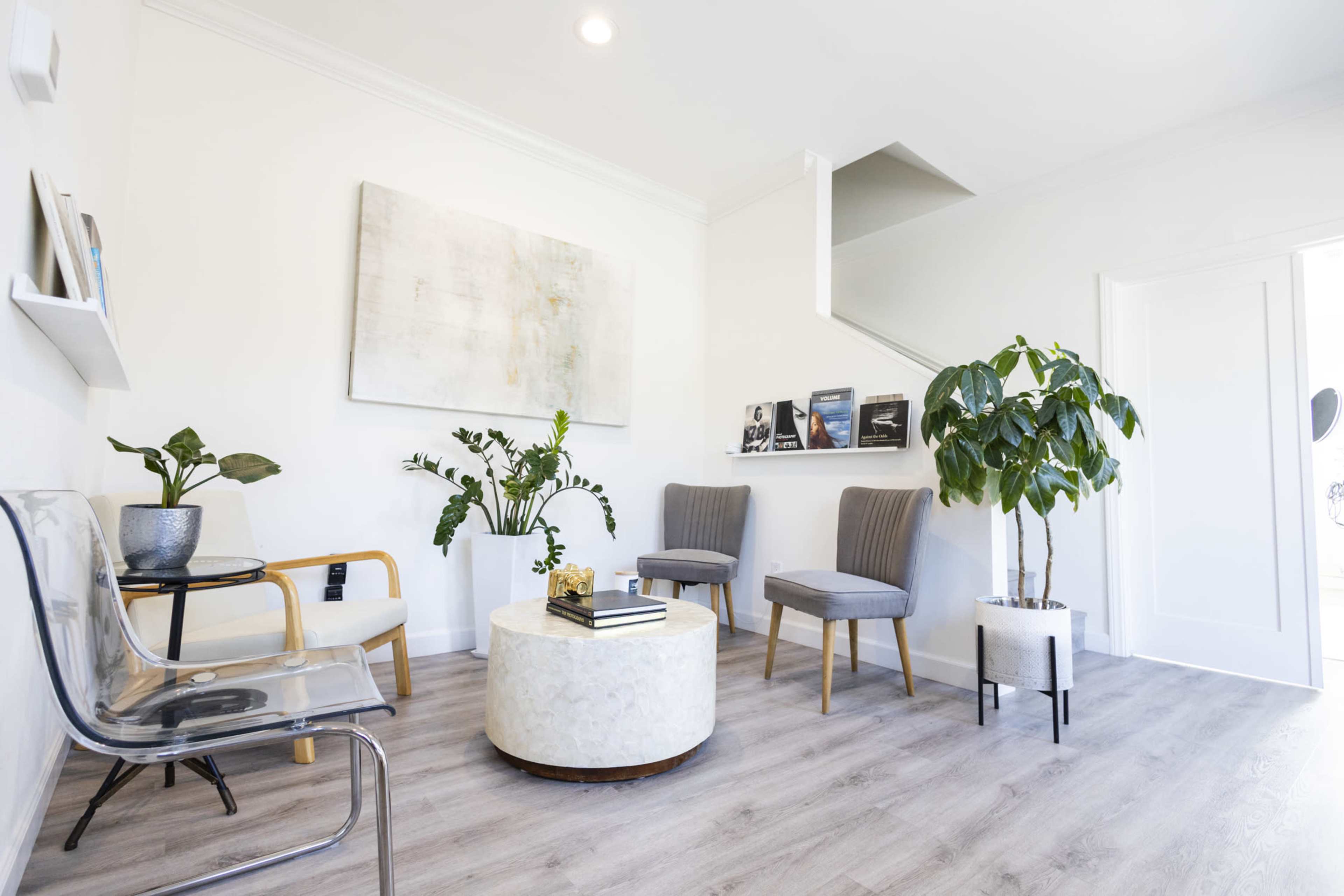 A bright, modern waiting area features a round white coffee table, potted plants, and a mix of upholstered and wooden seating.