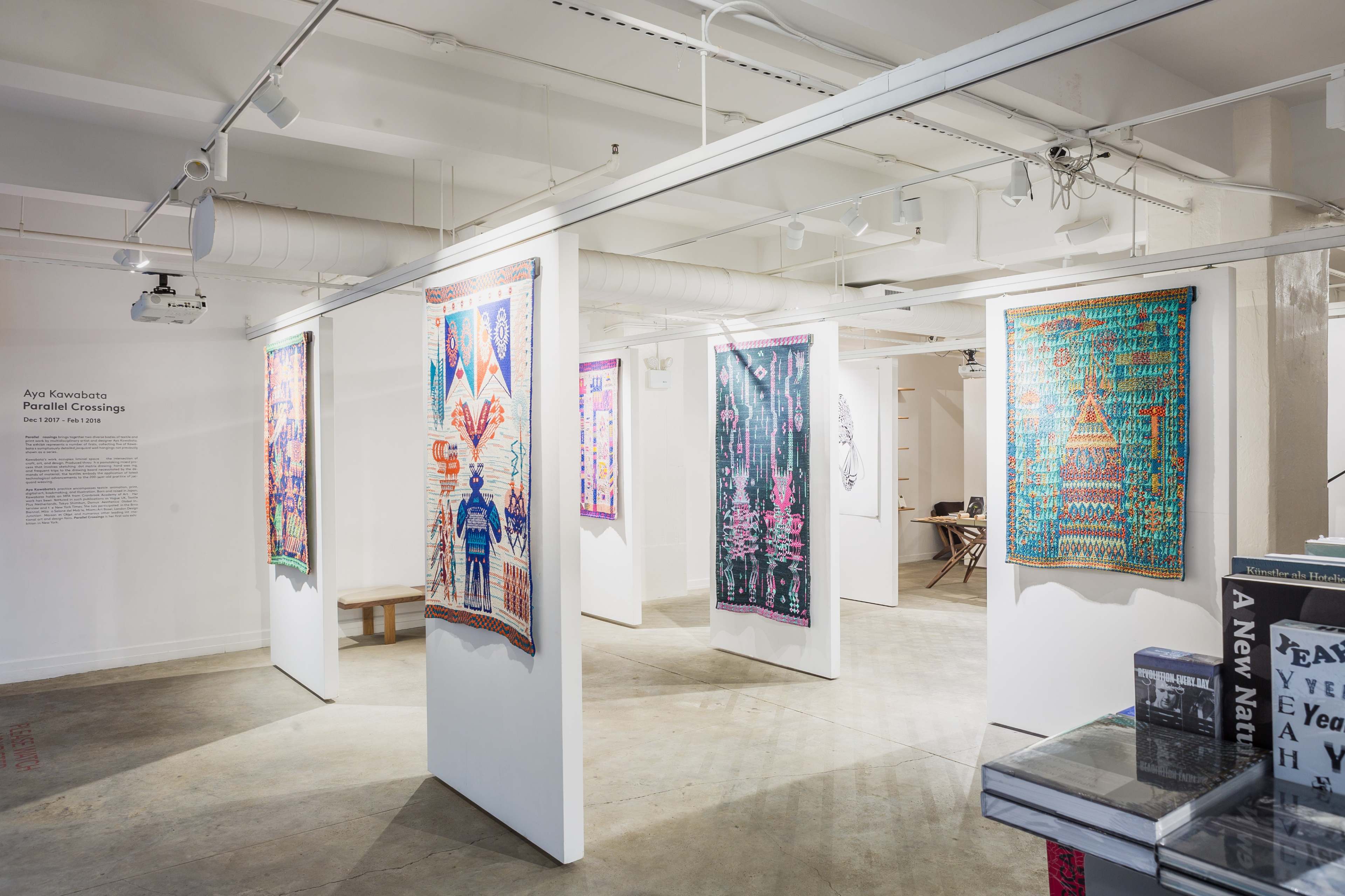 An art gallery with colorful textile artworks displayed on white walls, creating a vibrant exhibition space.
