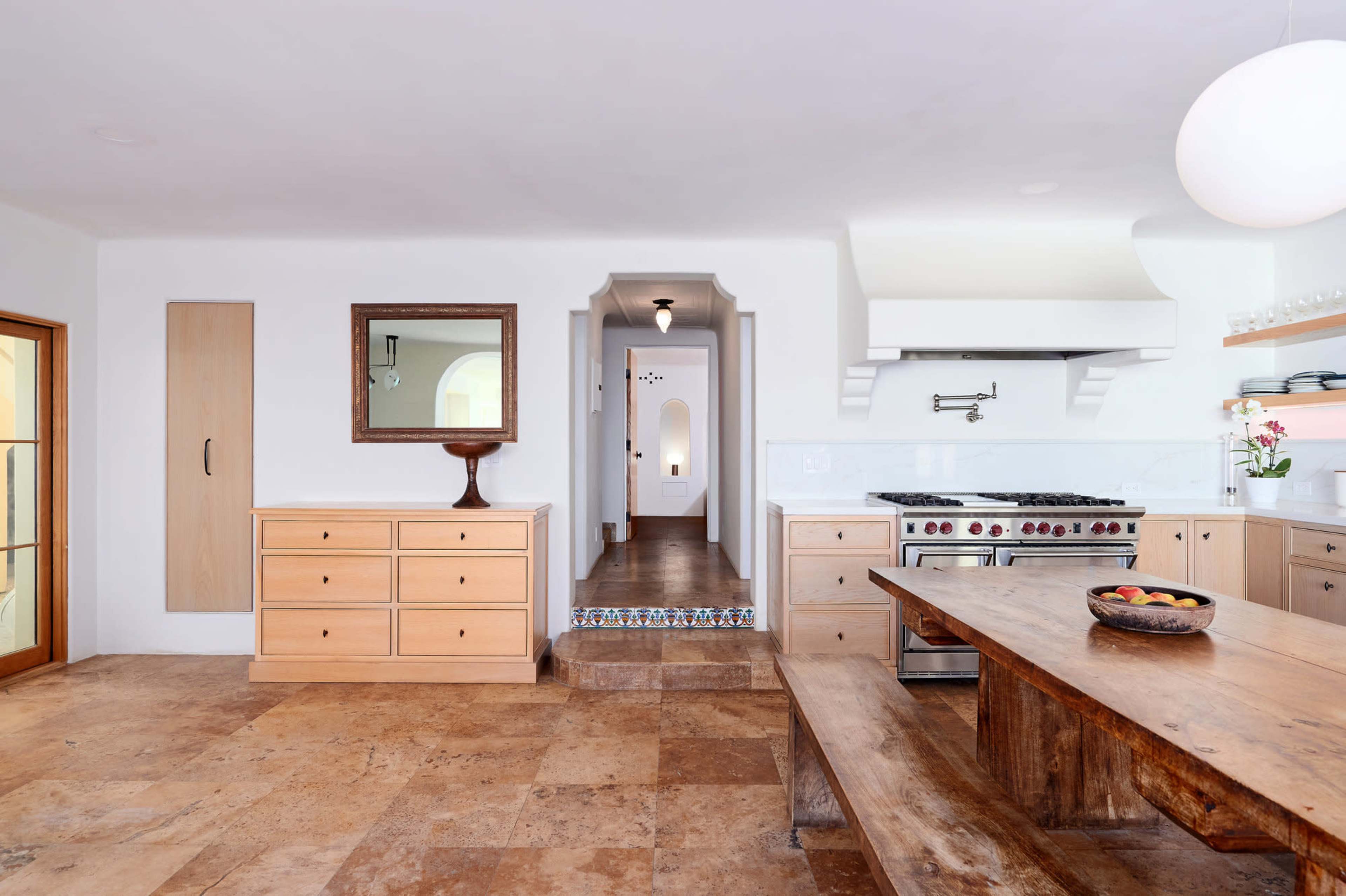 The kitchen features a wooden dining table, cream-colored cabinetry, and a doorway leading to a hallway with a decorative arch.