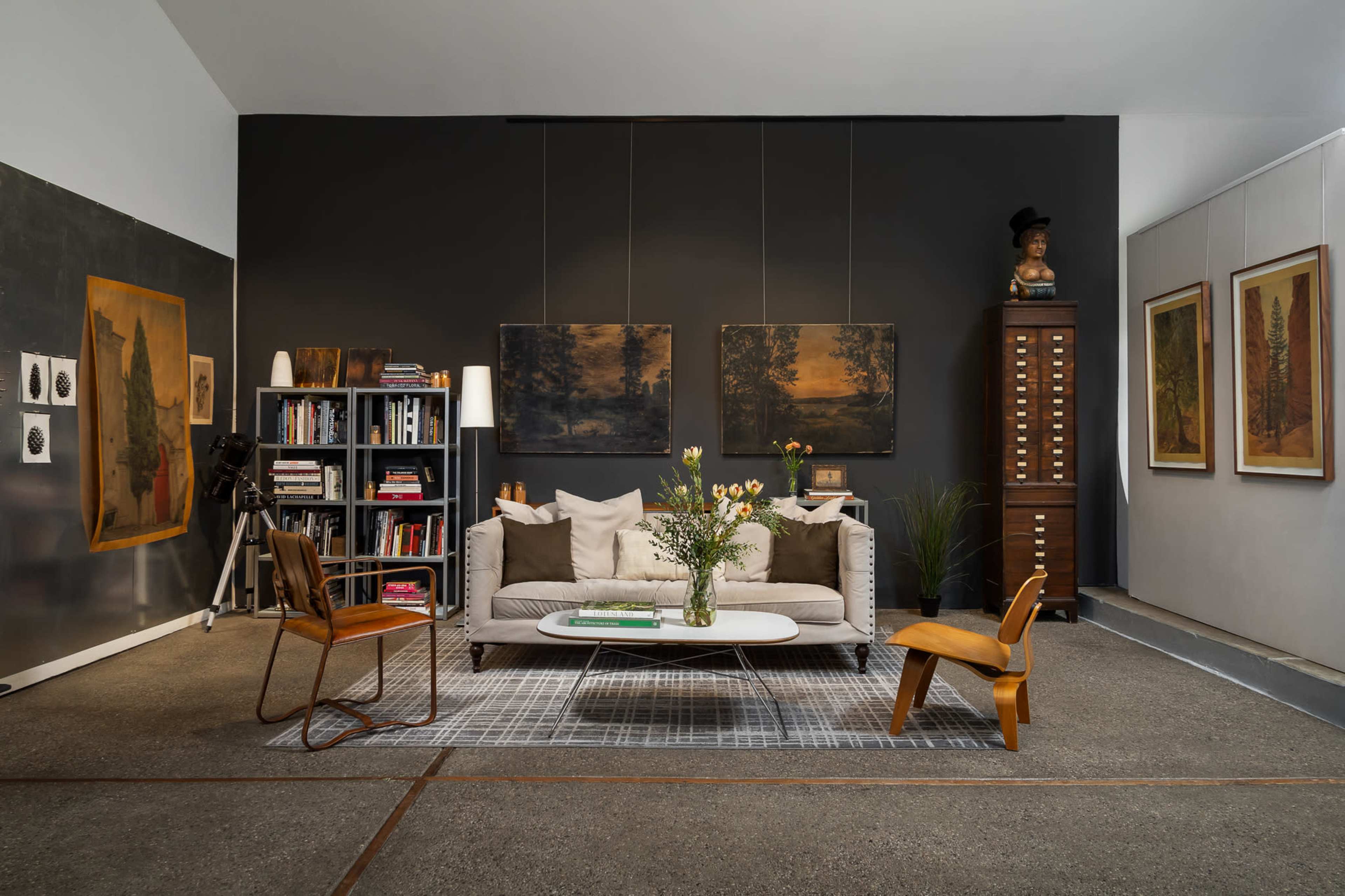 The image depicts a modern living room featuring a gray sofa, wooden chairs, a coffee table, and various artworks on the walls.