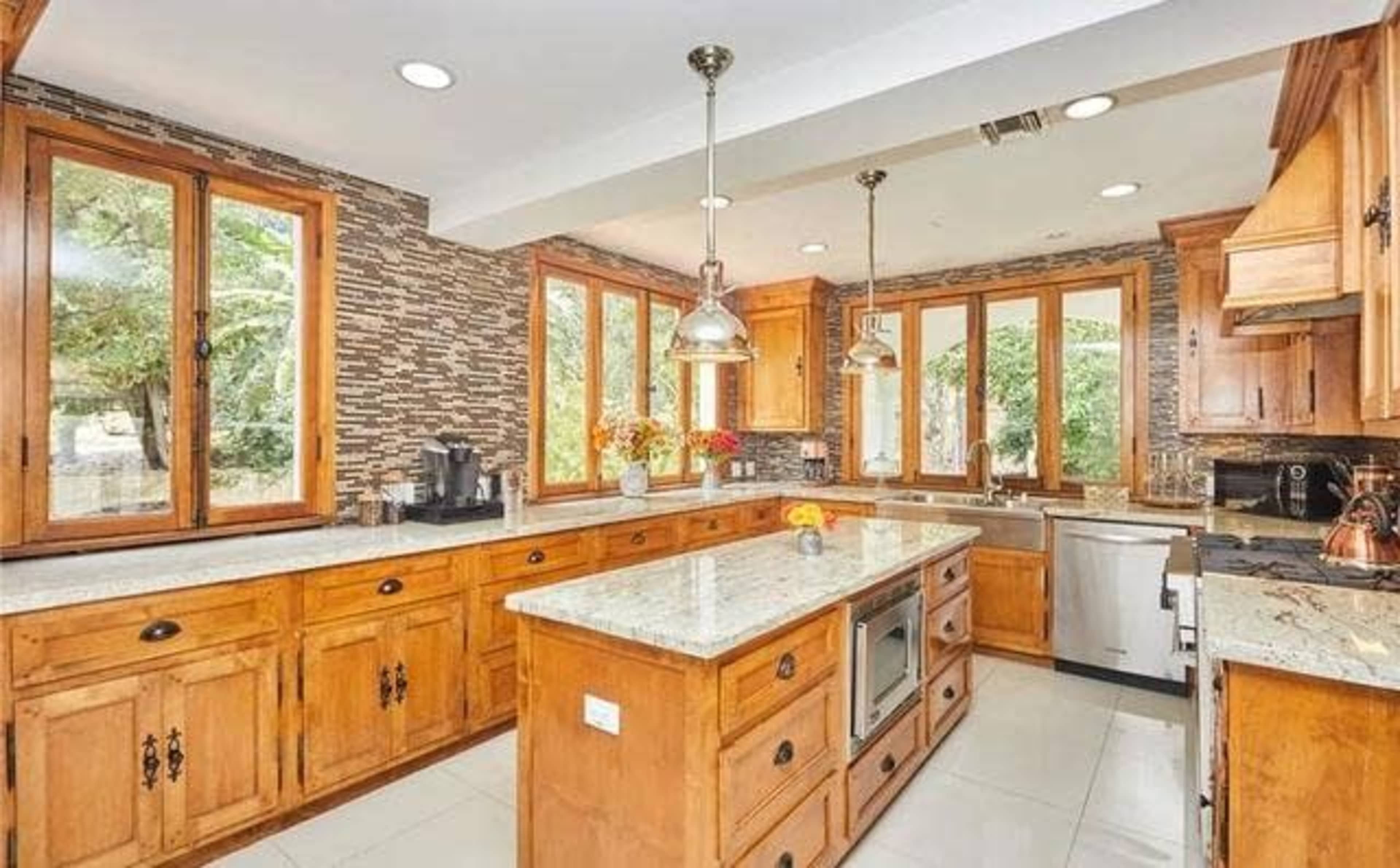 The kitchen features wooden cabinetry, granite countertops, and large windows that provide natural light.