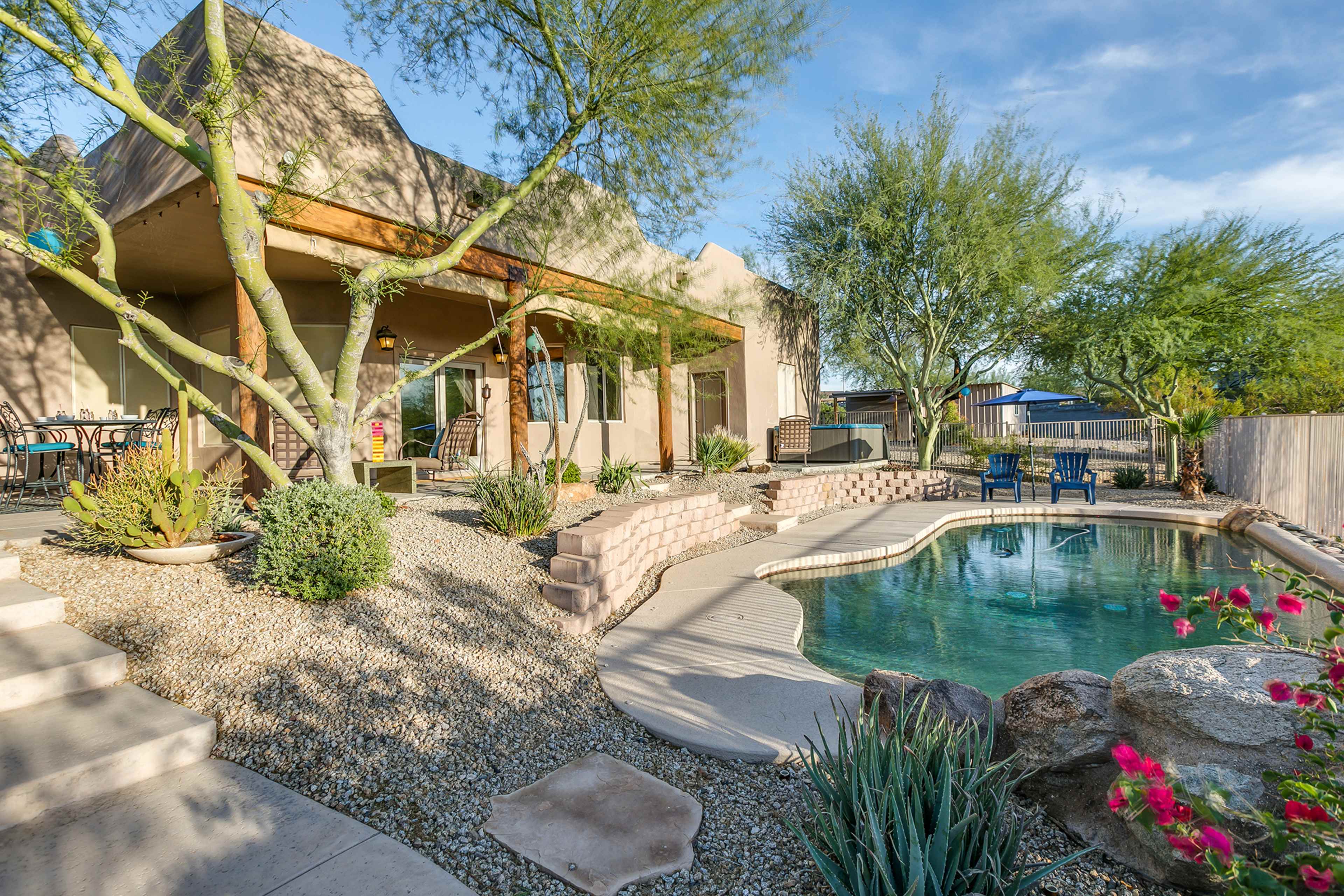 A landscaped backyard features a swimming pool surrounded by stone pathways, plants, and patio furniture.