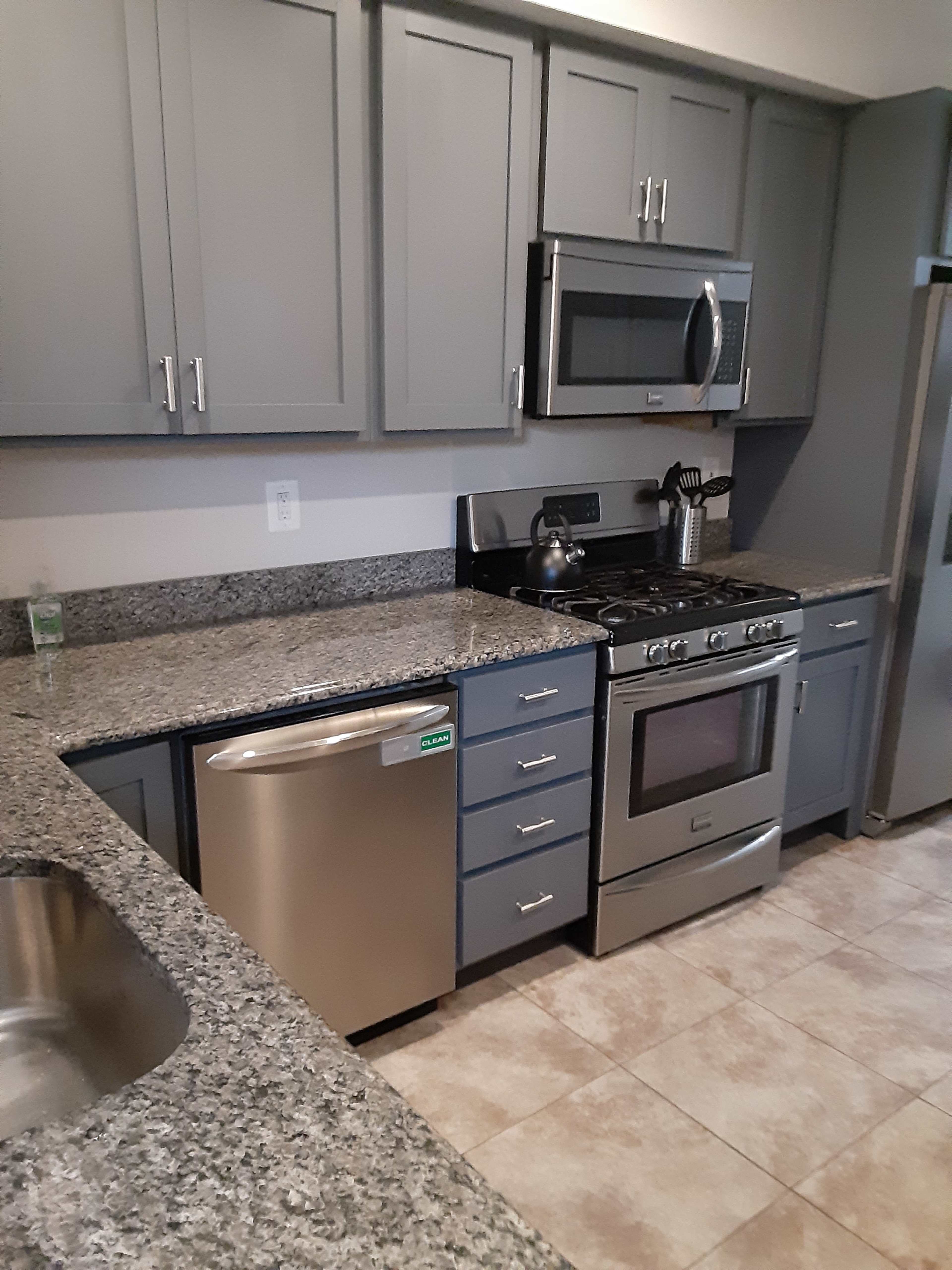 The kitchen features gray cabinets, granite countertops, a stainless steel stove and dishwasher, and tiled flooring.