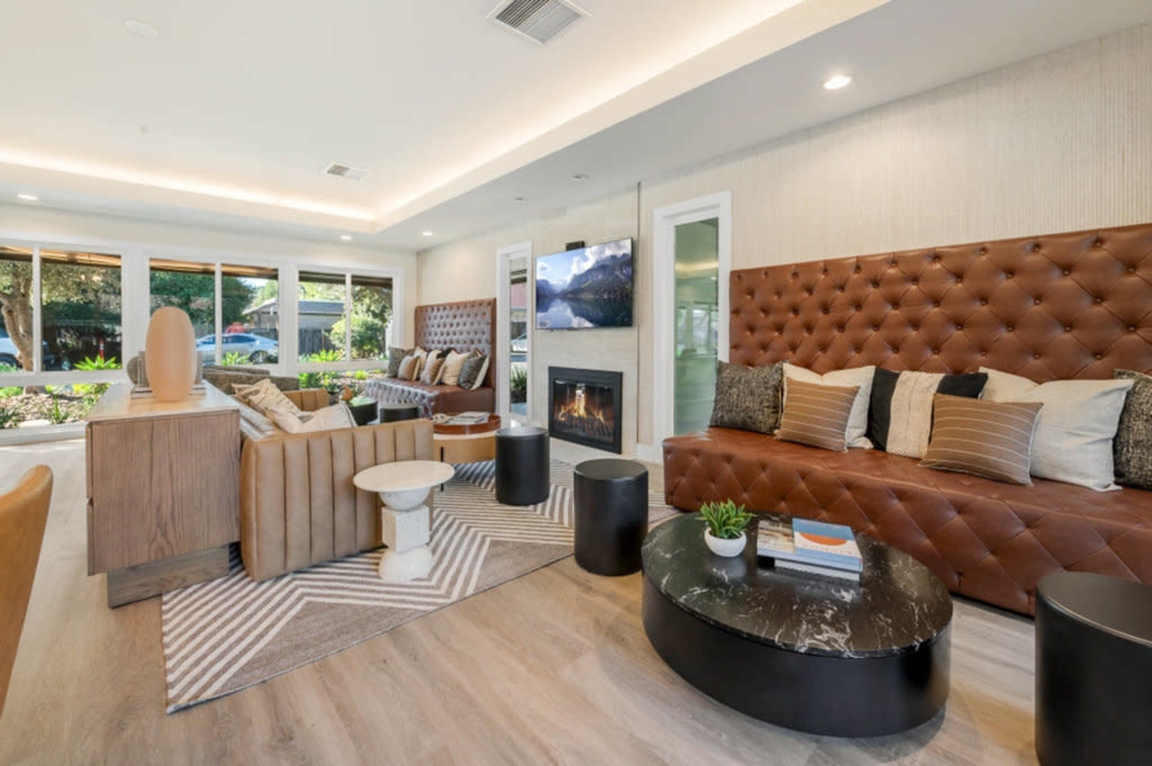 The image depicts a modern living room with leather tufted seating, a coffee table, and large windows allowing natural light to enter.