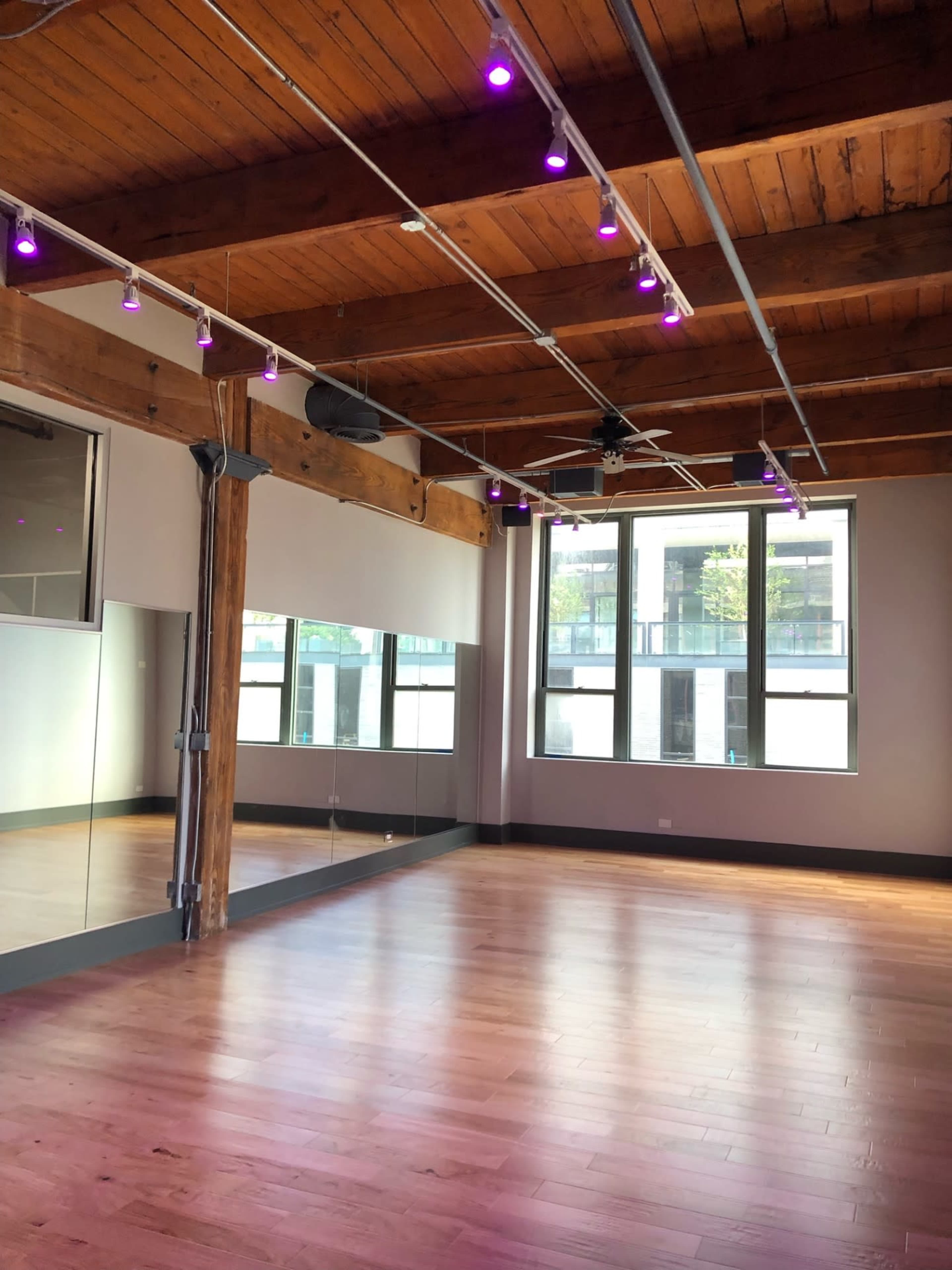 An empty studio space with wooden beams, a mirrored wall, and purple light fixtures.