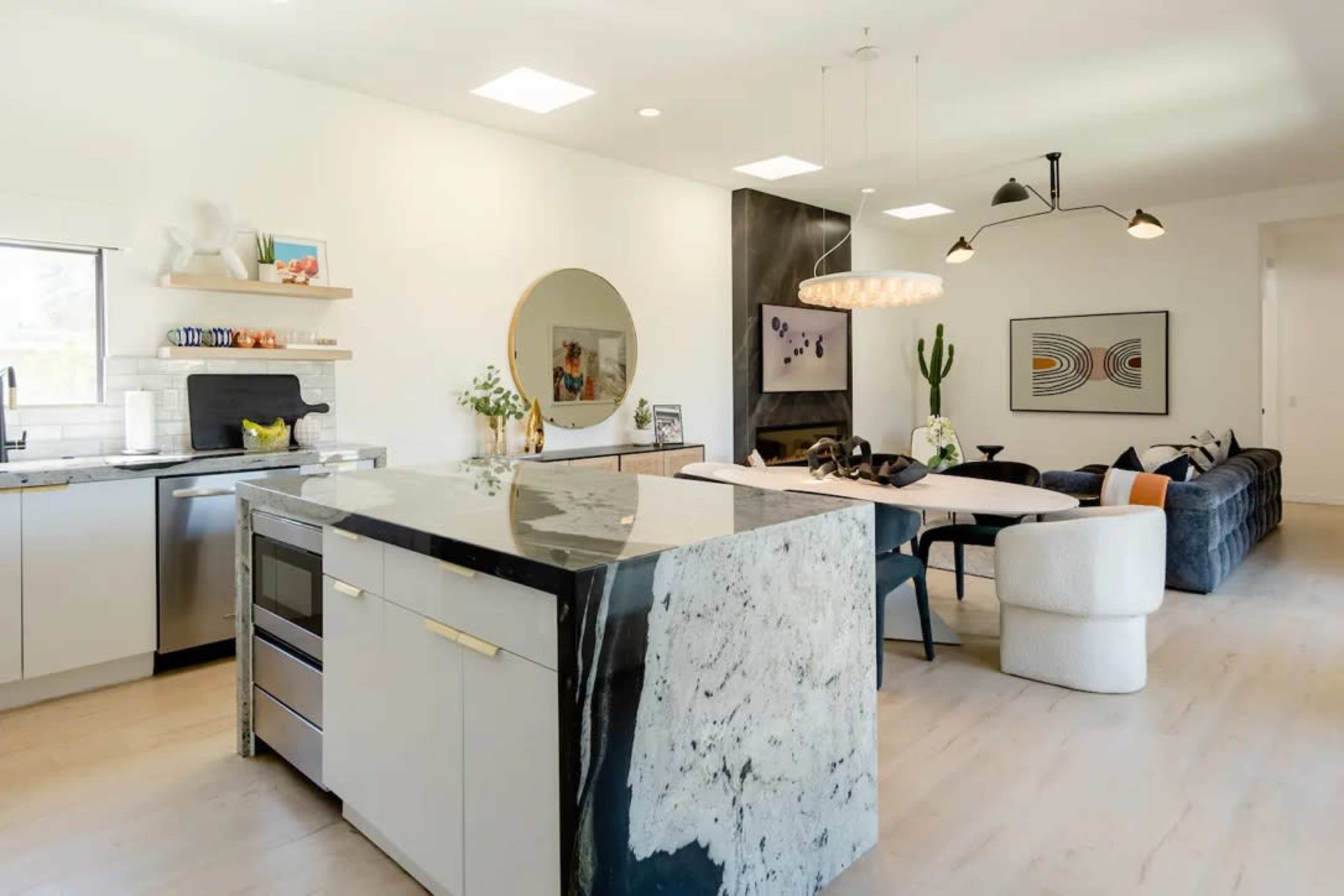 A modern kitchen features a large island with a marble countertop and sleek cabinetry, with an adjacent dining area furnished with contemporary seating and artwork.