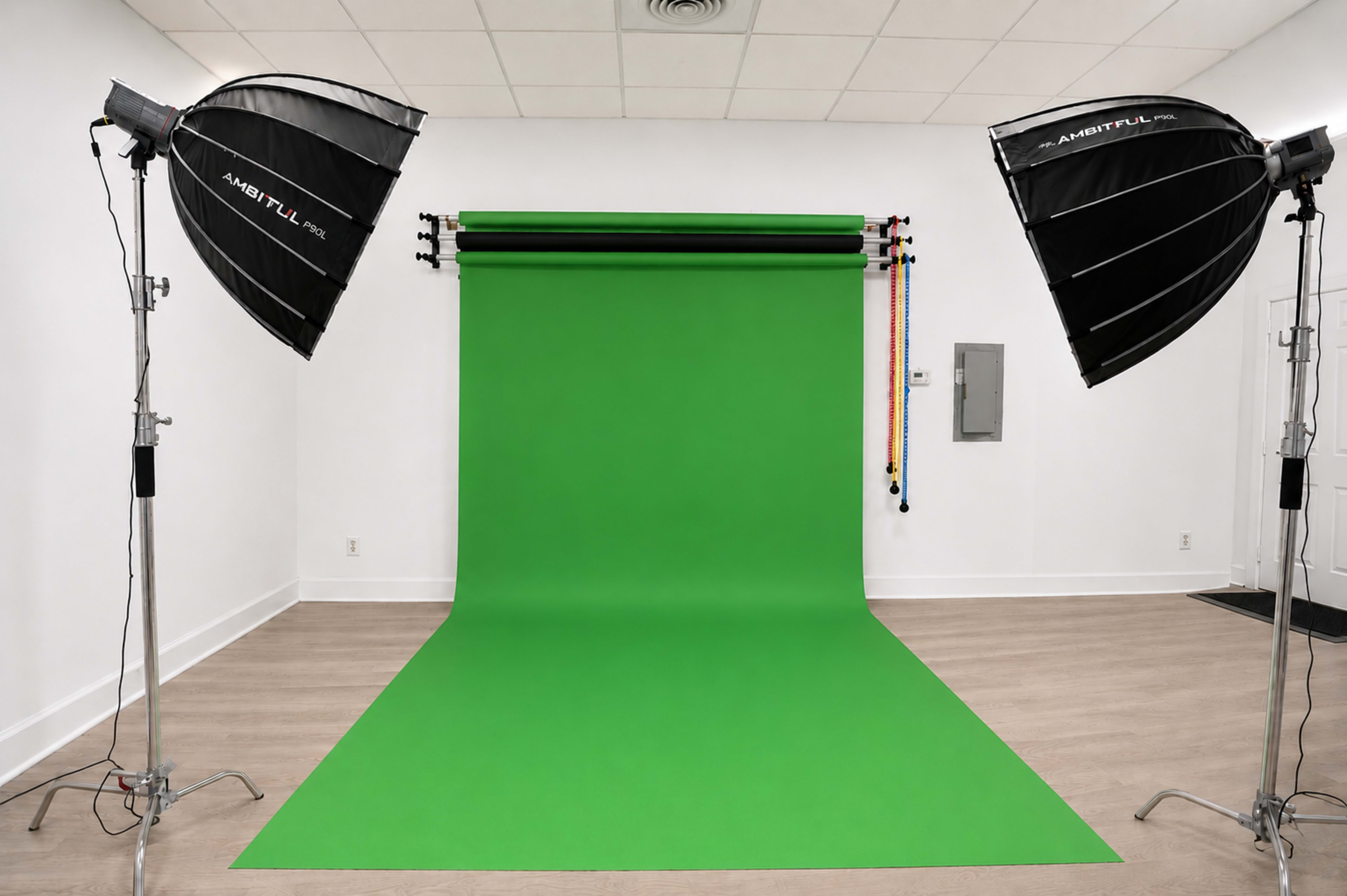 The image shows a photography studio featuring a green backdrop with two softbox lights on either side, all set against a plain white wall.