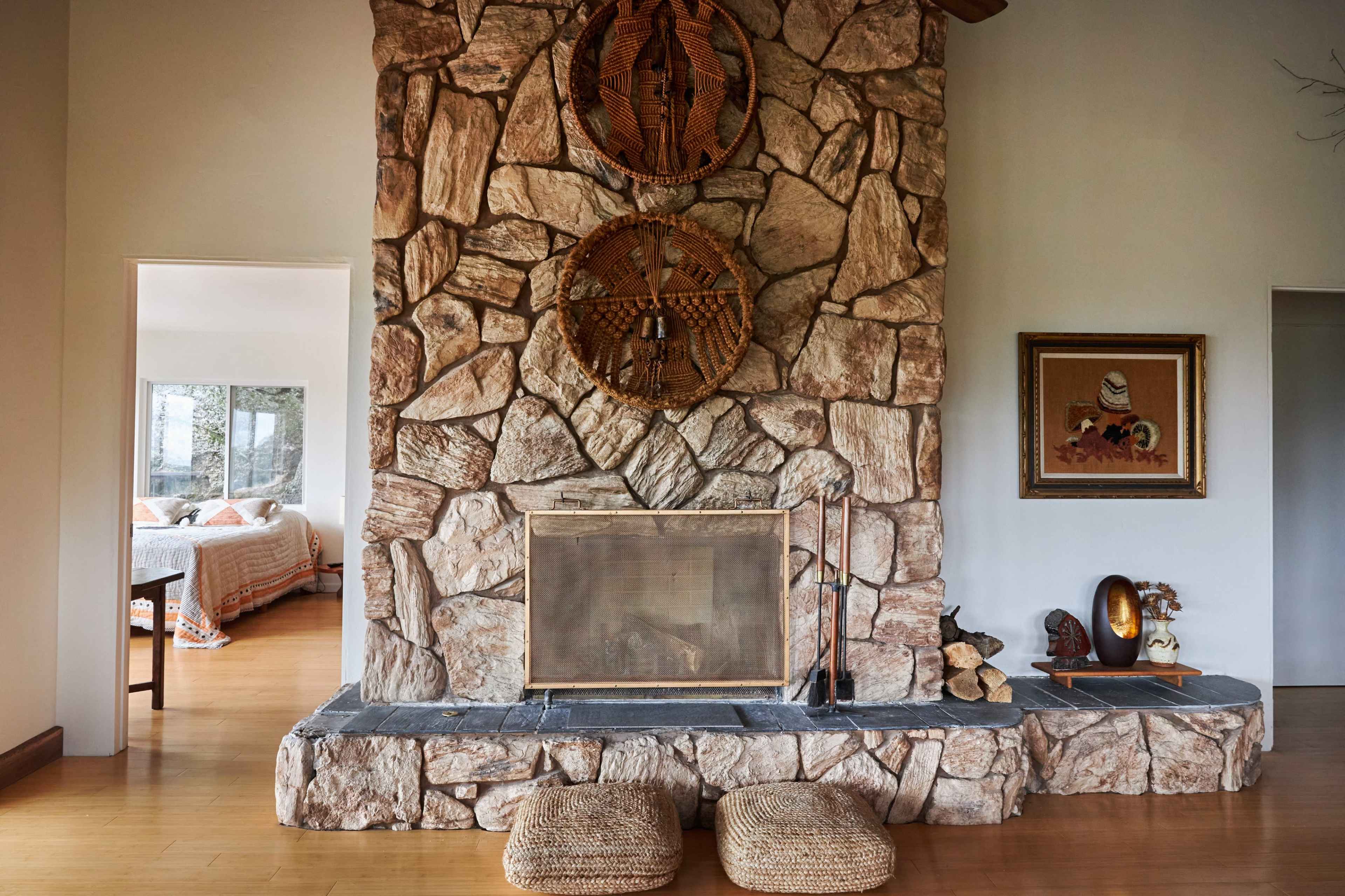 The image shows a stone fireplace adorned with woven baskets, with a view into a bedroom through an open doorway.