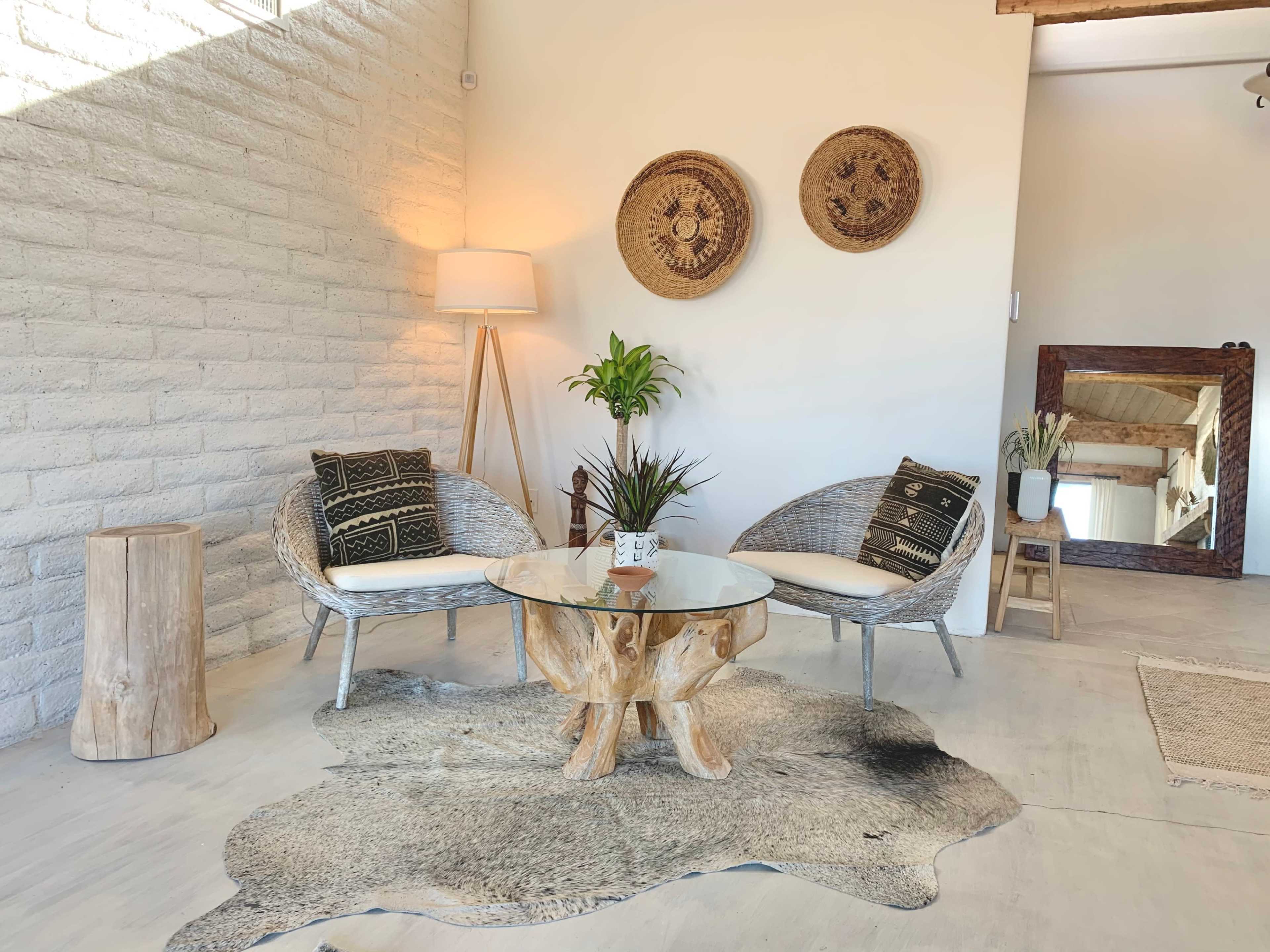 A cozy interior with two chairs, a round wooden coffee table, a plant, and decorative wall hangings in a well-lit space.