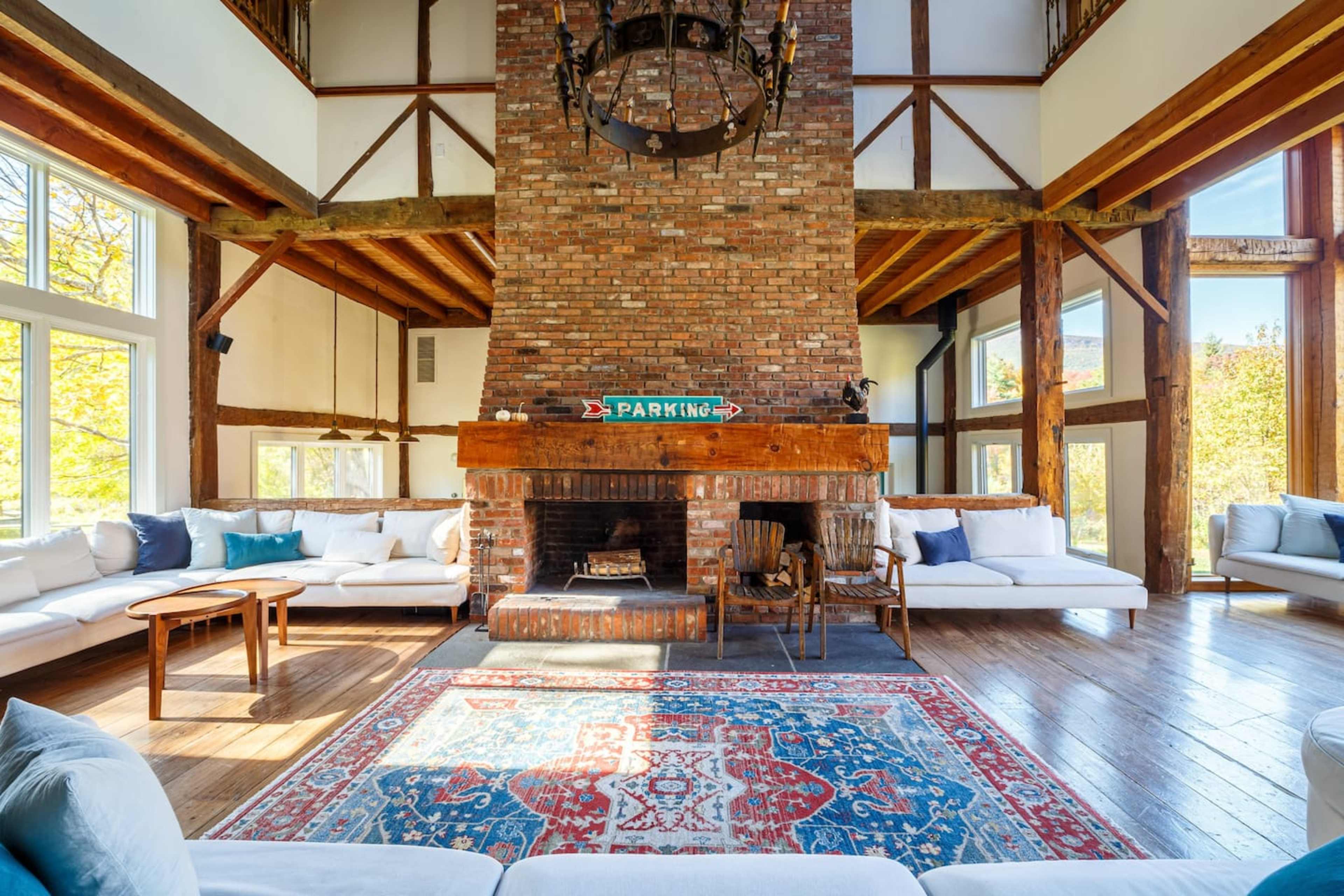 A spacious room with a large brick fireplace, wooden beams, and modern seating arranged around a decorative rug.