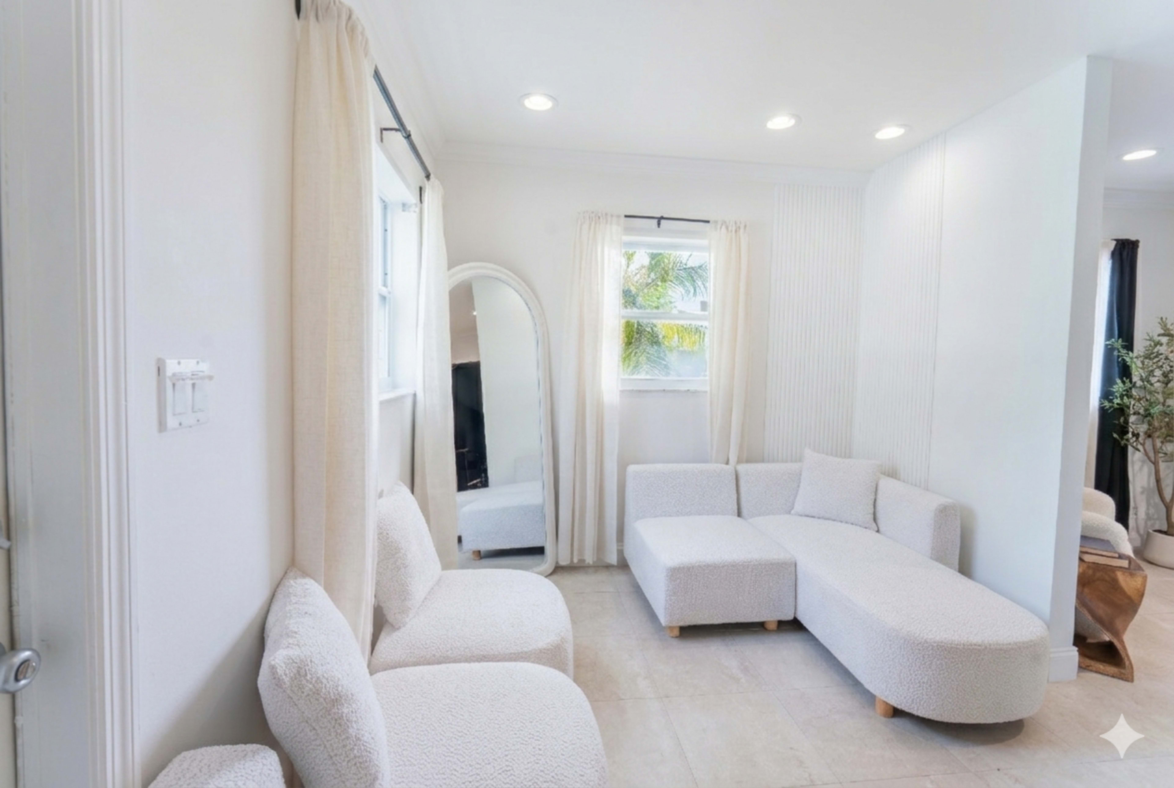 The image shows a light-colored modern living room with a curved sectional sofa, a large mirror, and a potted plant in the corner.