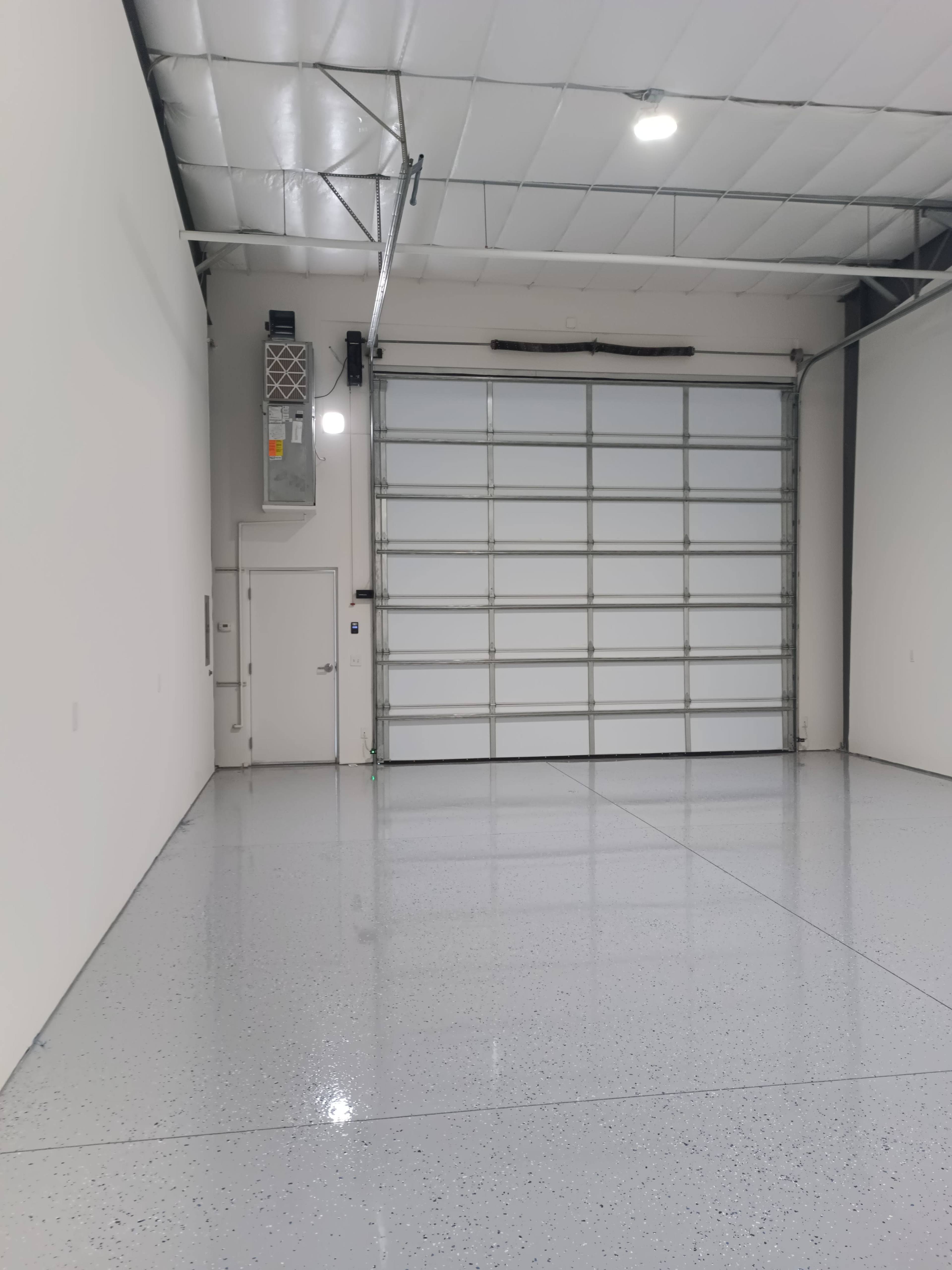 The image shows a spacious, clean garage with a large overhead door and a shiny, smooth floor.