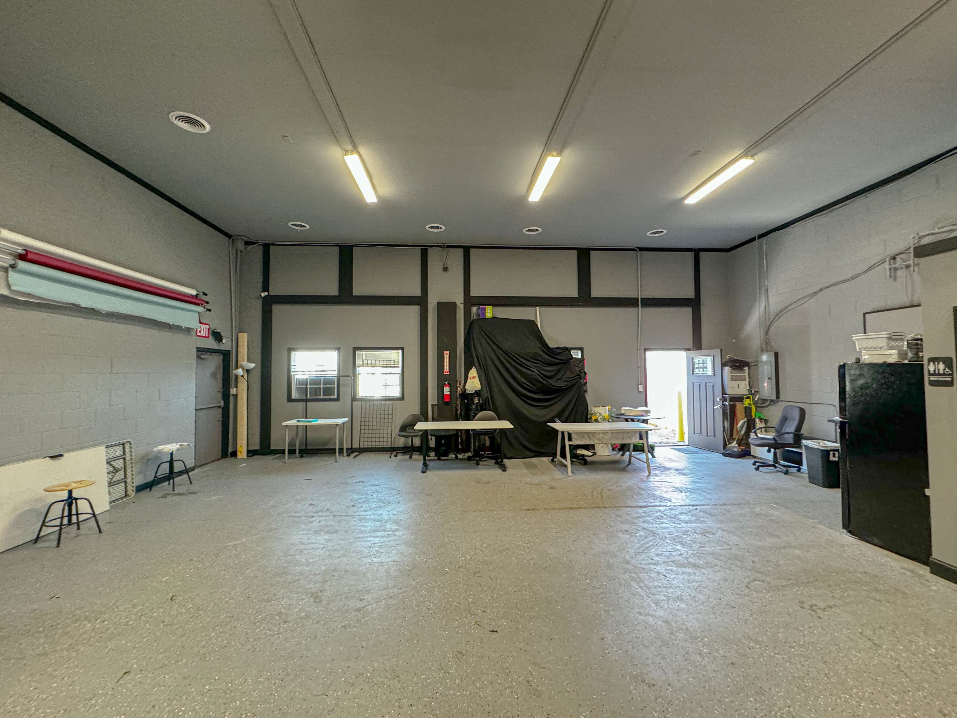 A spacious, empty room featuring minimal furniture, including several tables and chairs, with a black curtain obscuring part of the back wall.