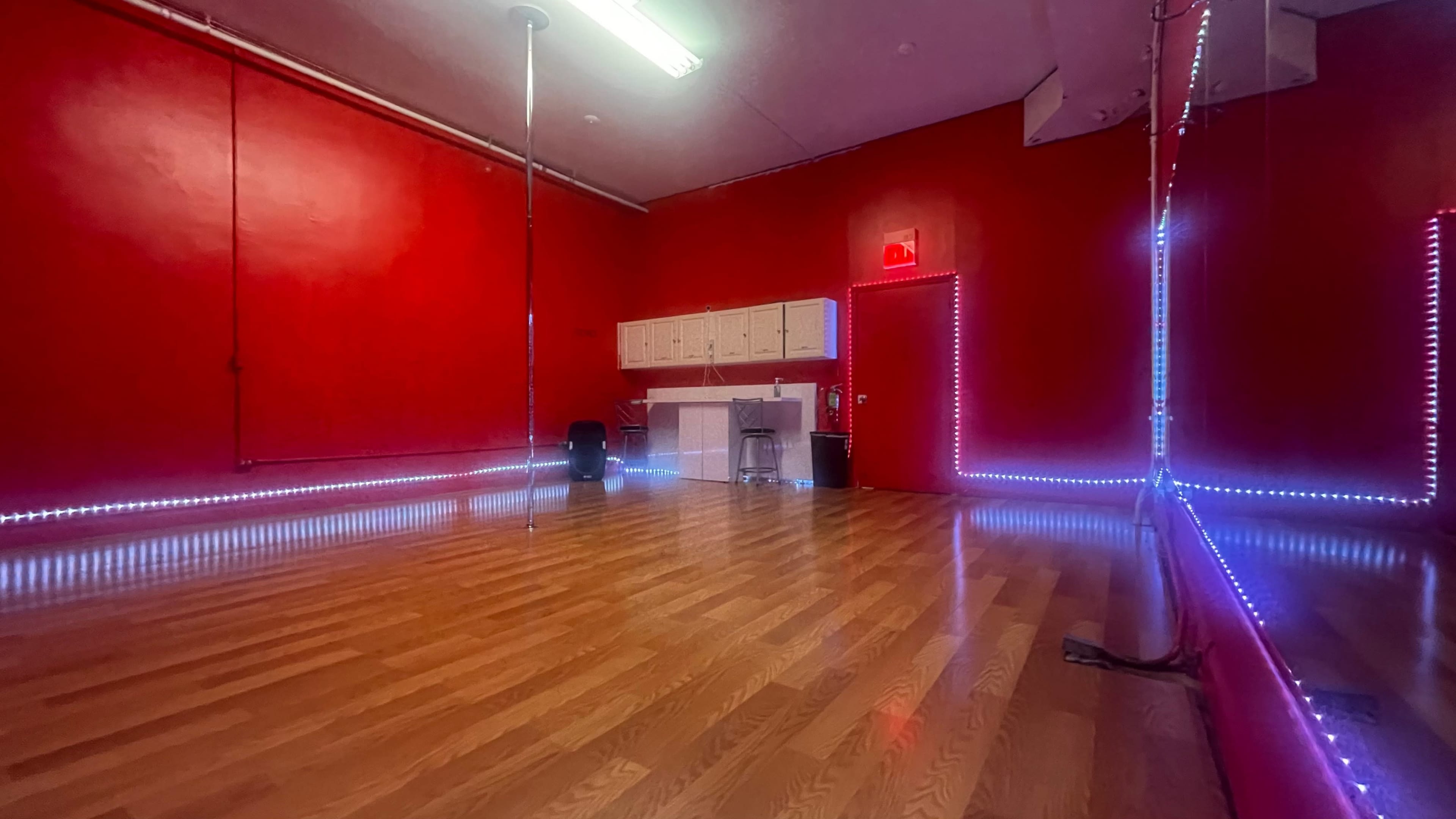 A red-walled room with a polished wooden floor, a pole in the center, and illuminated edges along the walls.